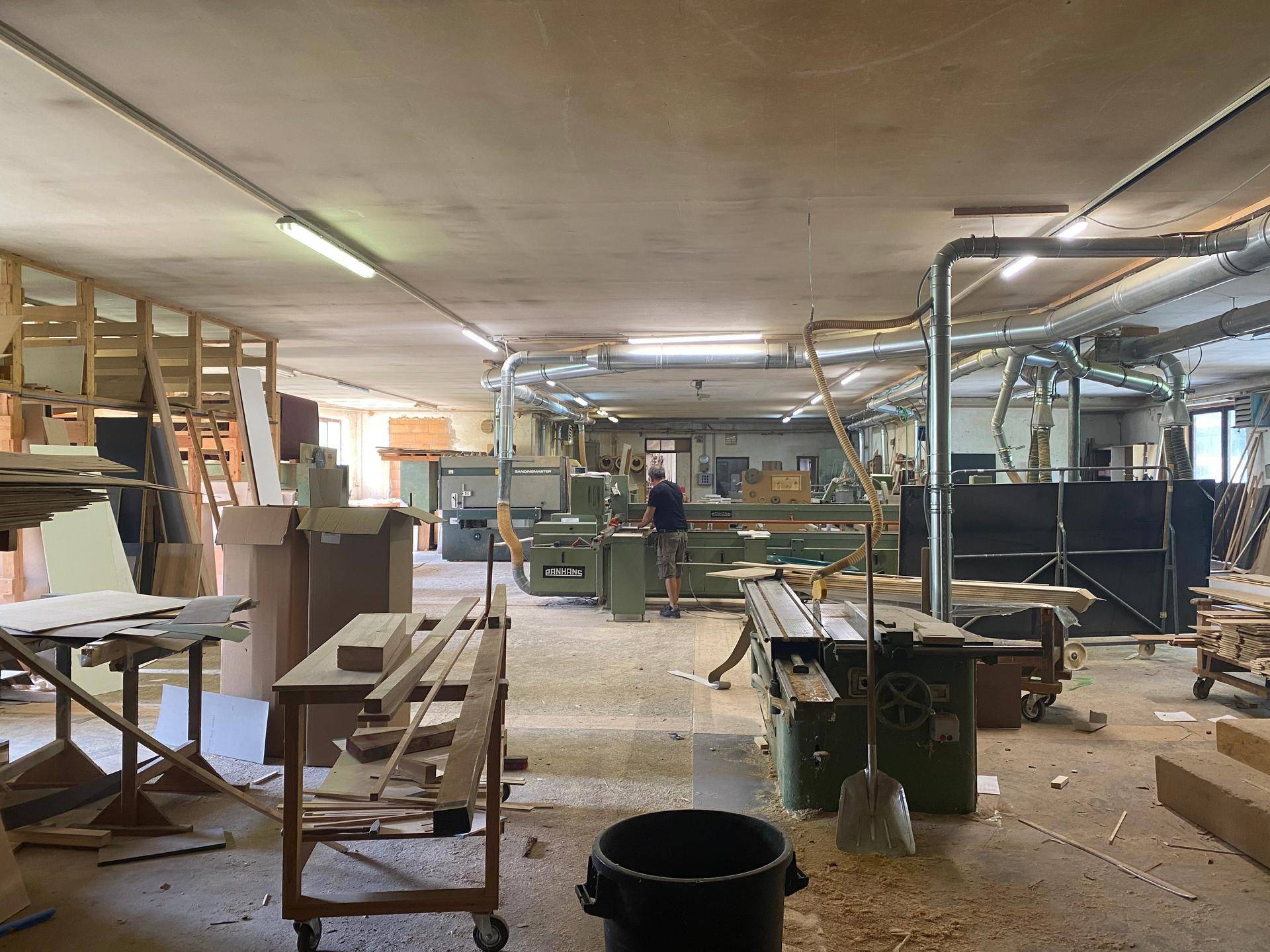 Geräumige Holzwerkstatt mit industriellen Maschinen, Absaugsystemen und Holzmaterialien für die Bearbeitung.