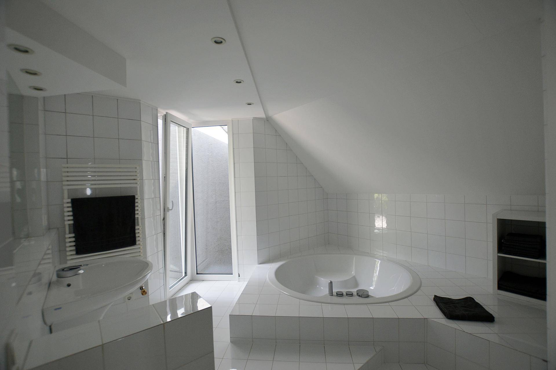 Helles Badezimmer im Dachgeschoss mit runder Badewanne und weißen Fliesen.