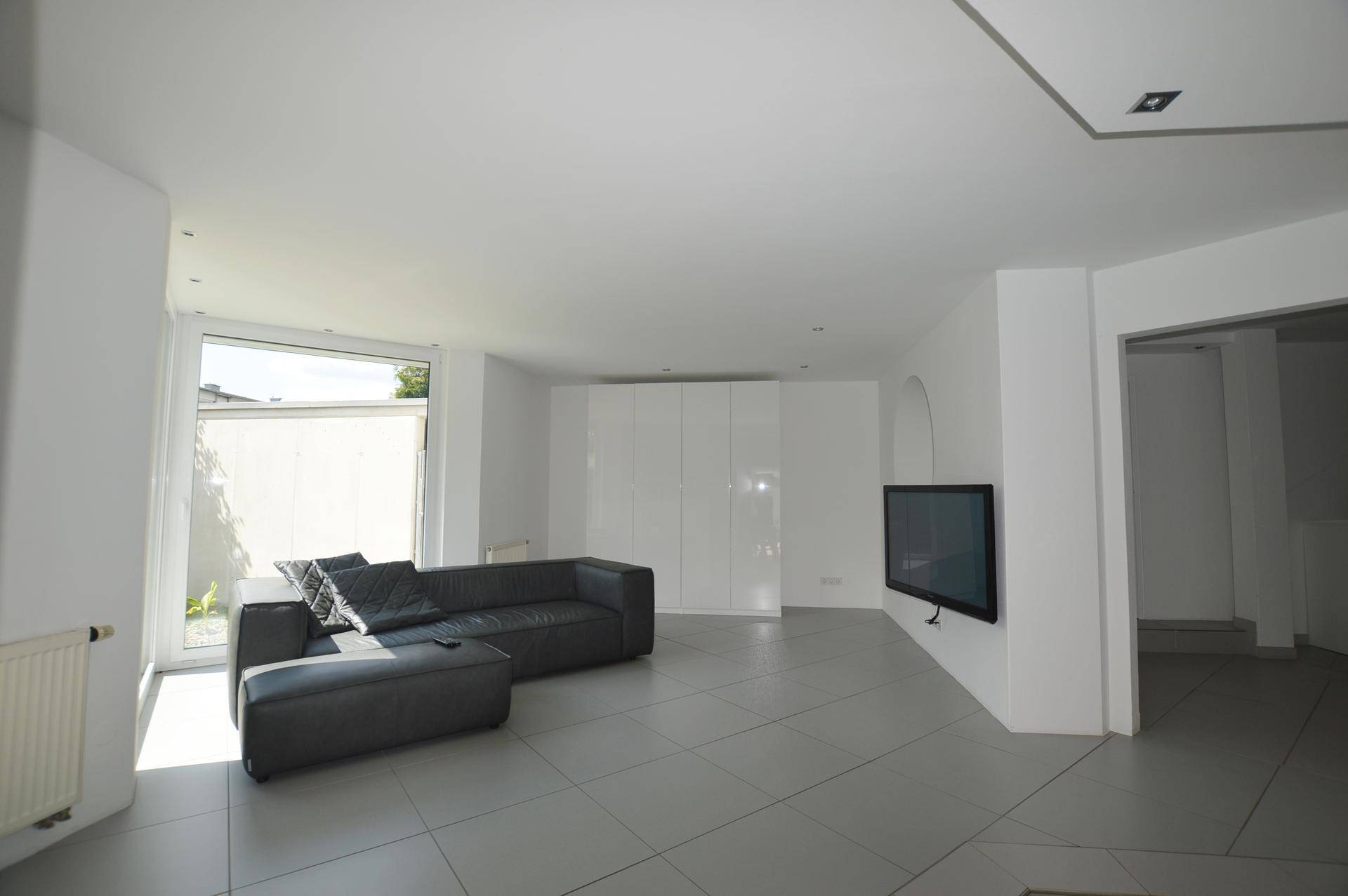 Helles Wohnzimmer mit modernem Sofa, Fliesenboden und integrierten Schränken.