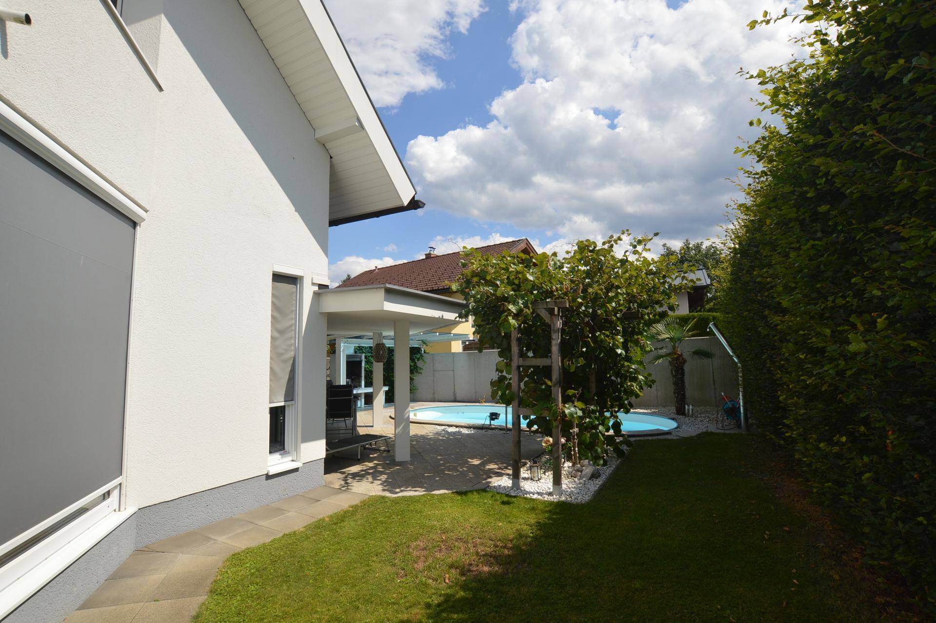 Gepflegter Gartenbereich mit Rasenfläche, Bäumen und Zugang zur überdachten Terrasse.