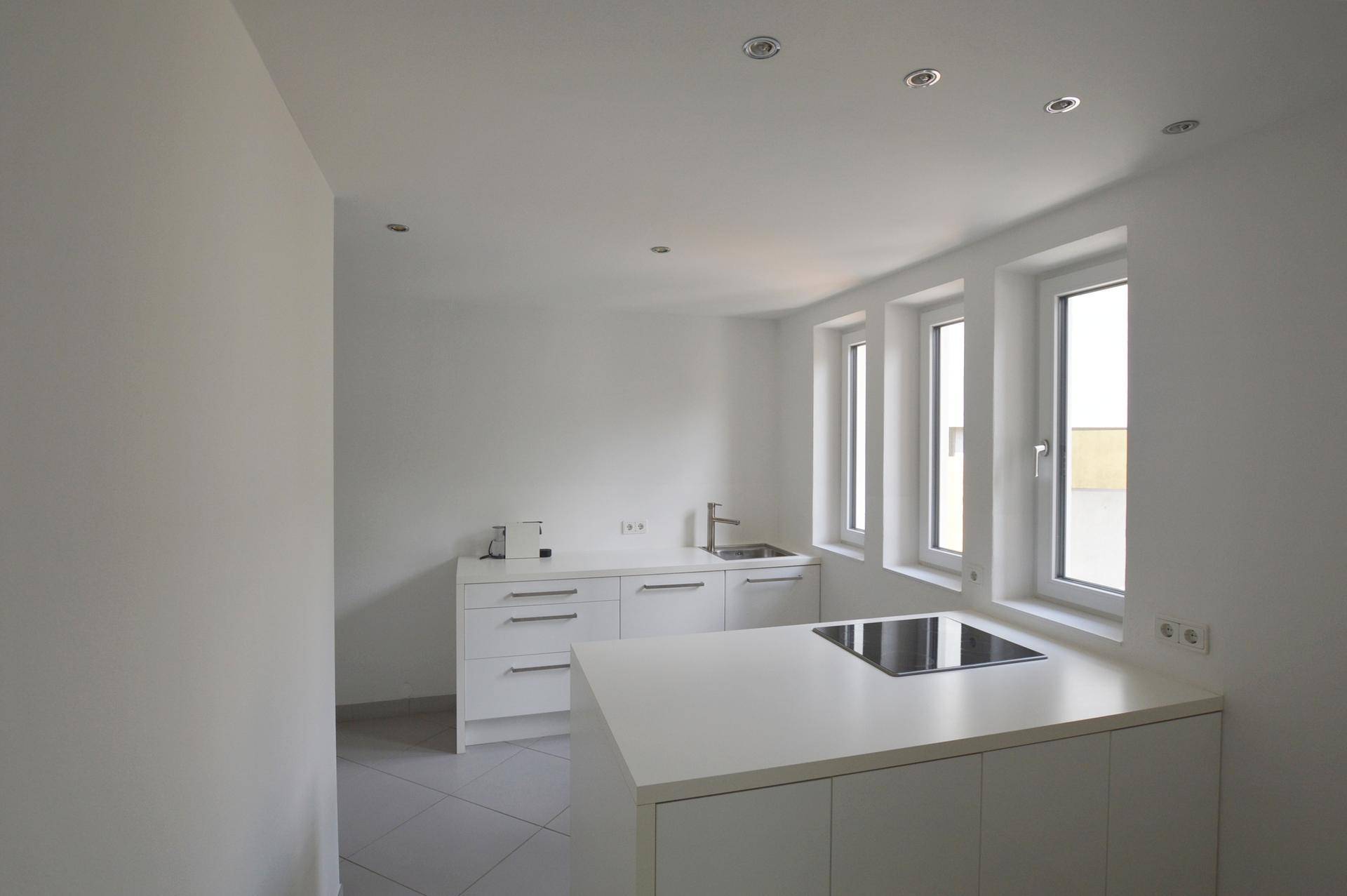 Moderne weiße Küche mit Kochinsel, Induktionskochfeld und mehreren Fenstern.