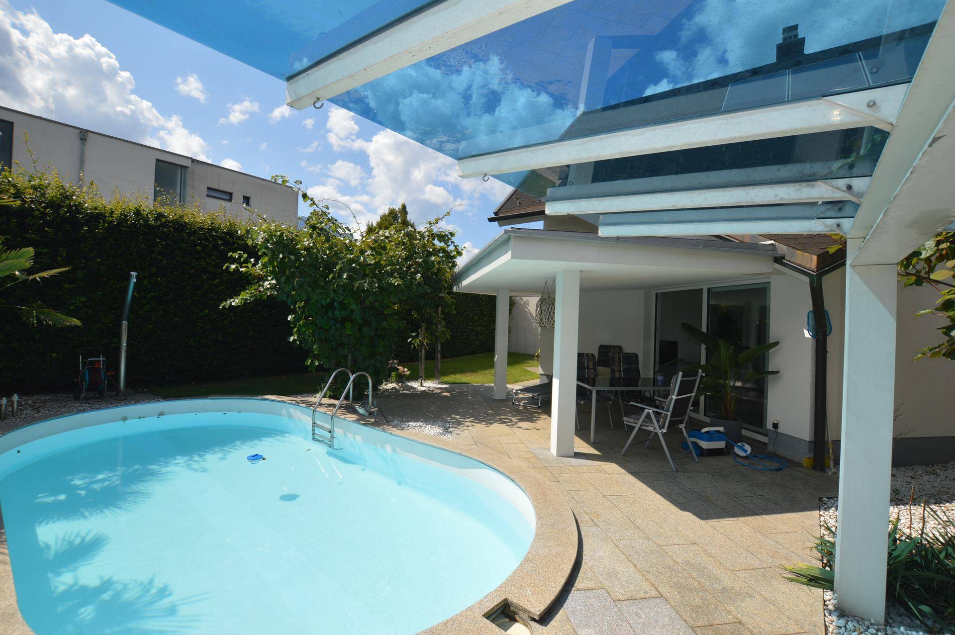 Außenbereich mit ovalem Swimmingpool, Sonnenterrasse und Glasüberdachung.
