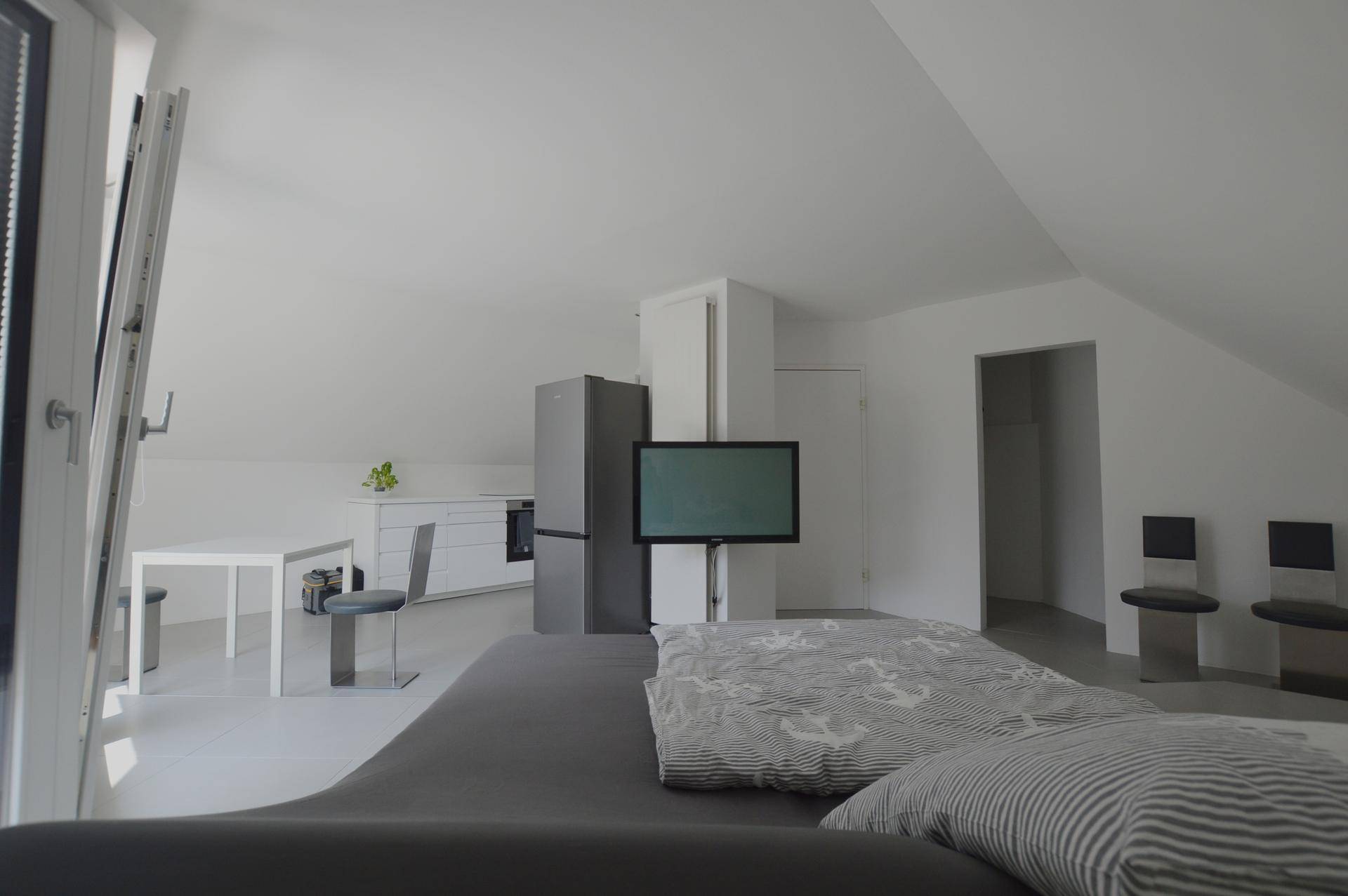 Helles Schlafzimmer im Dachgeschoss mit integrierter Küchenzeile und Fernseher.