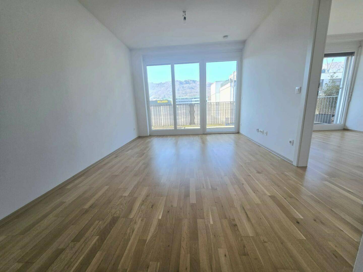 Lichtdurchfluteter Raum mit Holzboden und bodentiefen Fenstern, die einen schönen Ausblick auf die Umgebung bieten.