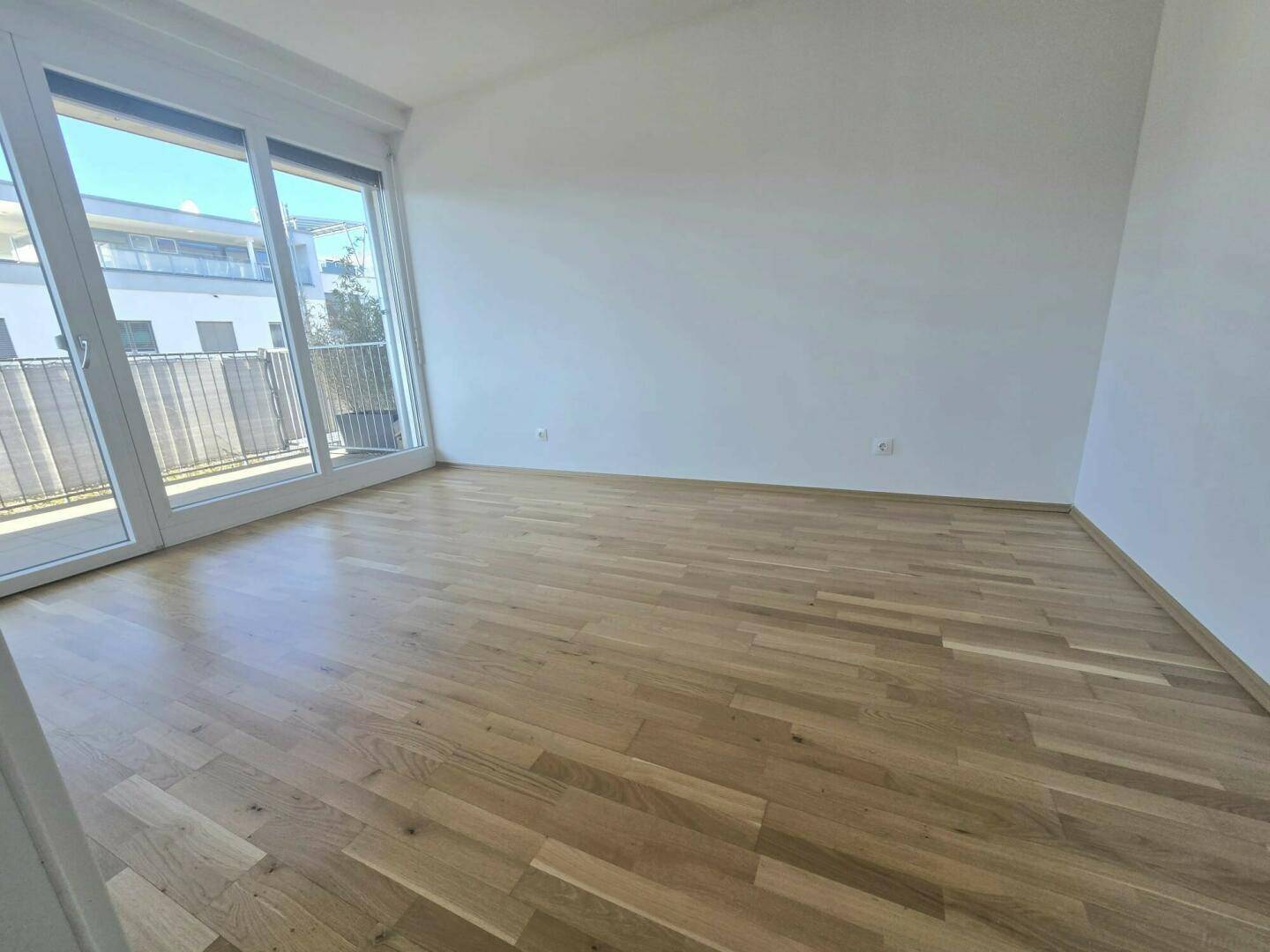 Lichtdurchflutetes Zimmer mit Holzboden und breiten Fenstern, die einen direkten Zugang zum Außenbereich ermöglichen.