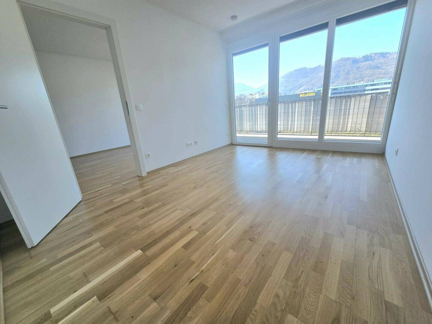 Helles Schlafzimmer mit Parkettboden und großen Fenstern, die Zugang zu einem sonnigen Balkon bieten.