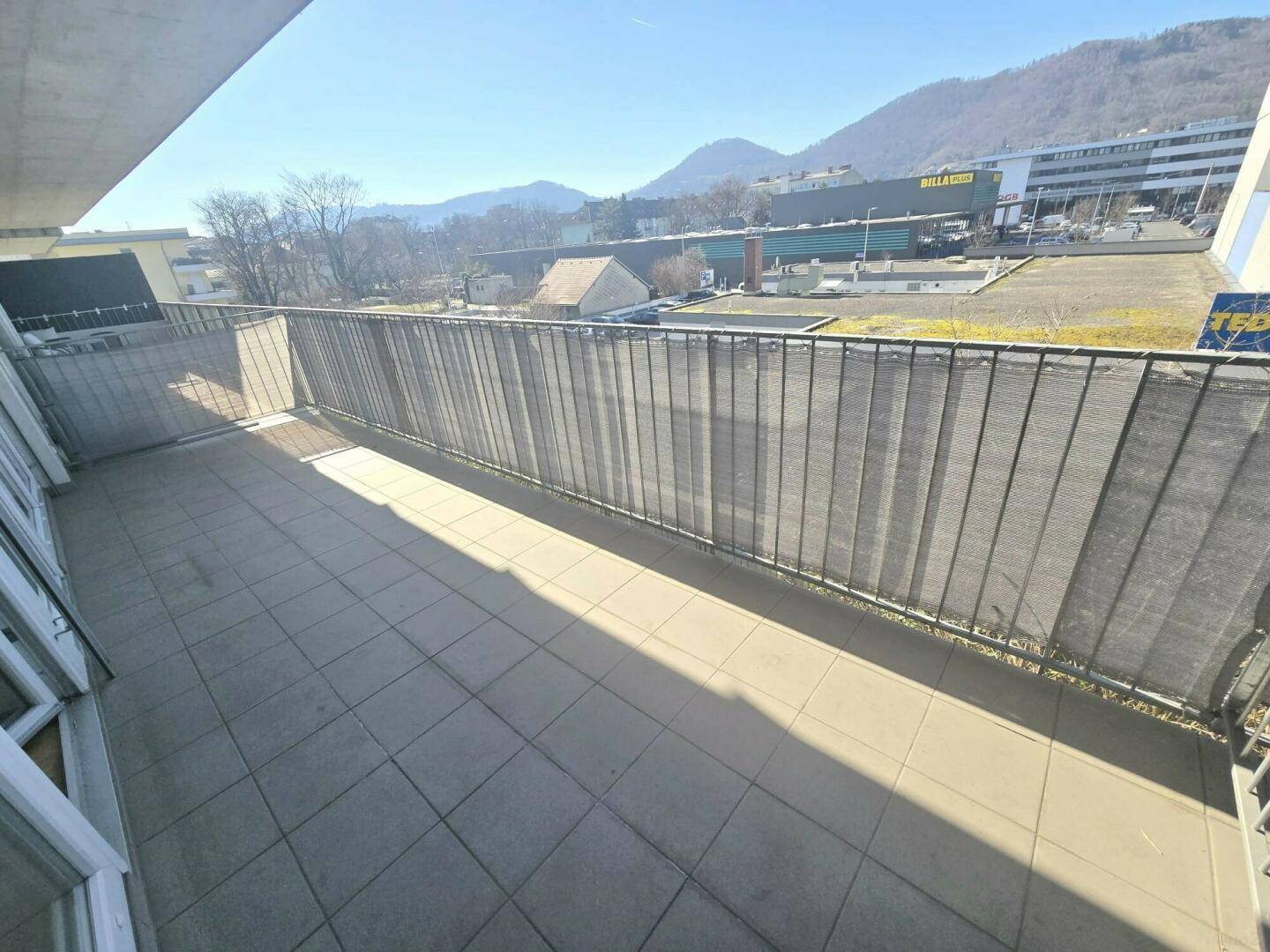 Geräumiger Balkon mit Fliesenboden und weitem Blick auf die Berge und die umliegende Bebauung.