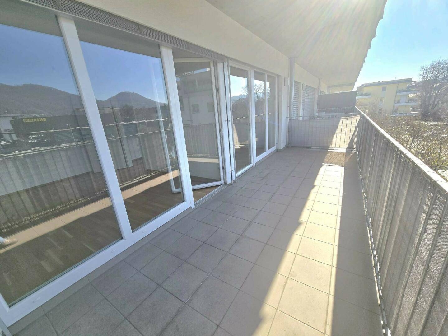 Sonniger Balkon mit Fliesenboden und großzügigen Glasfronten, ideal zum Entspannen im Freien.
