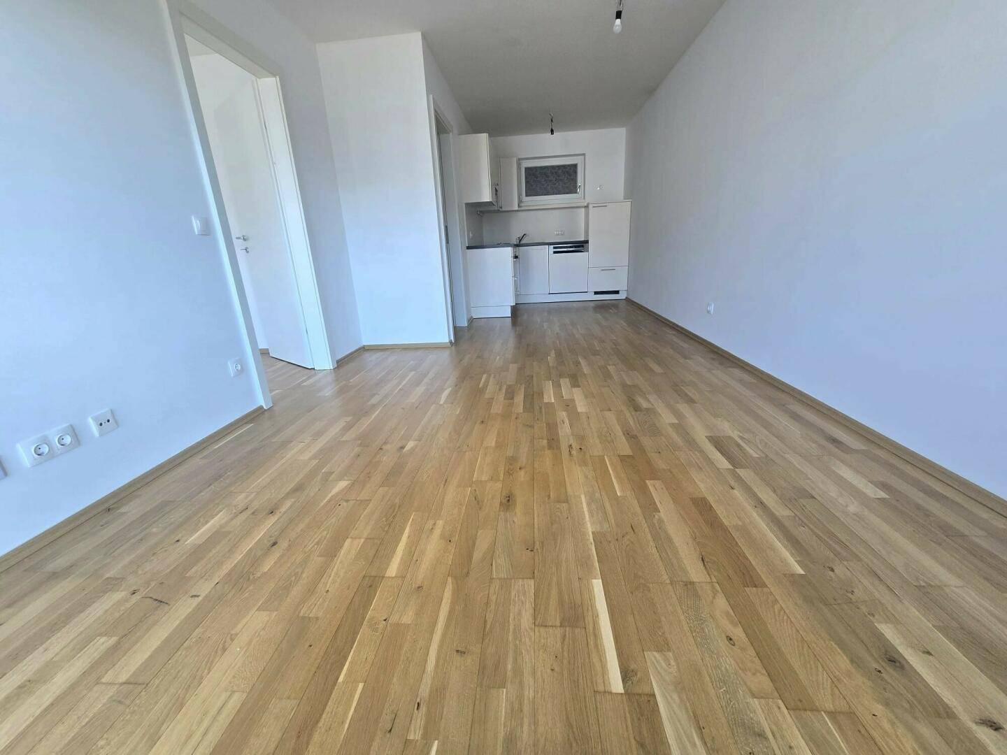 Geräumiger Wohnbereich mit hellem Holzfußboden und offener Sicht zur Küche, ideal für modernes Wohnen.