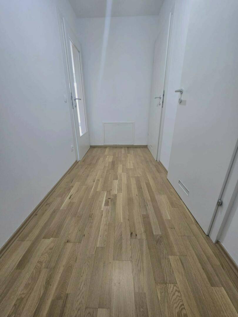 Schmaler Flur mit hellem Holzfußboden und weißen Wänden, der zu verschiedenen Räumen führt.