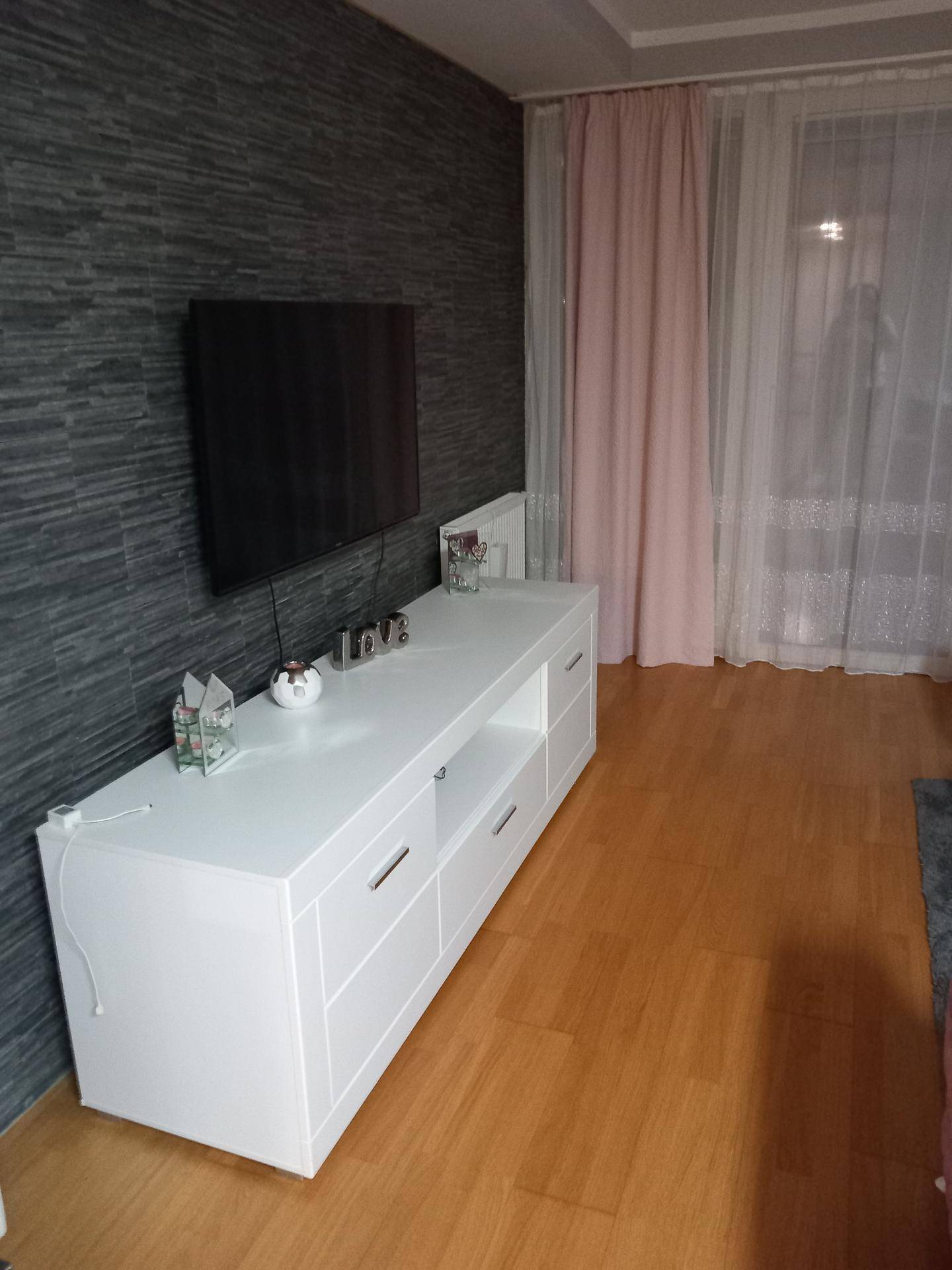 Wohnzimmerbereich mit dunkler Akzentwand, weißem TV-Möbel und Laminatboden.