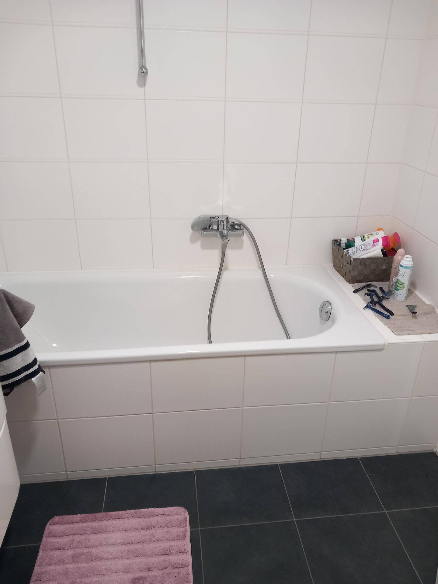 Badezimmer mit eingebauter Badewanne, weißen Wandfliesen und dunklem Fliesenboden.