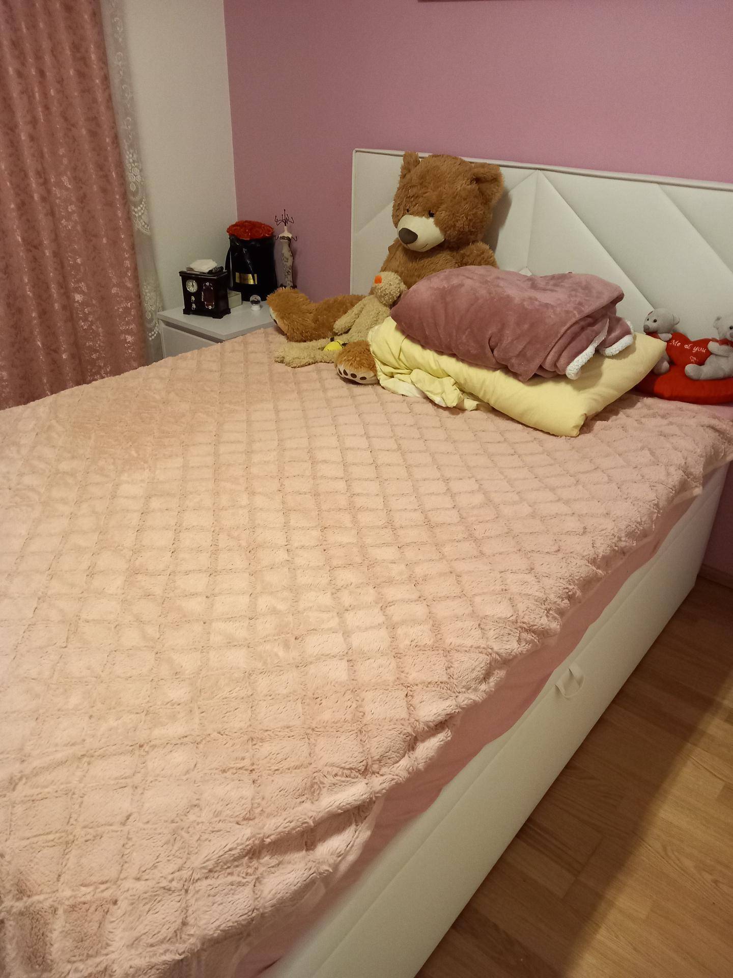 Schlafzimmer mit großem Bett, rosa Bettwäsche und Wandfarbe, dekoriert mit Plüschtieren.