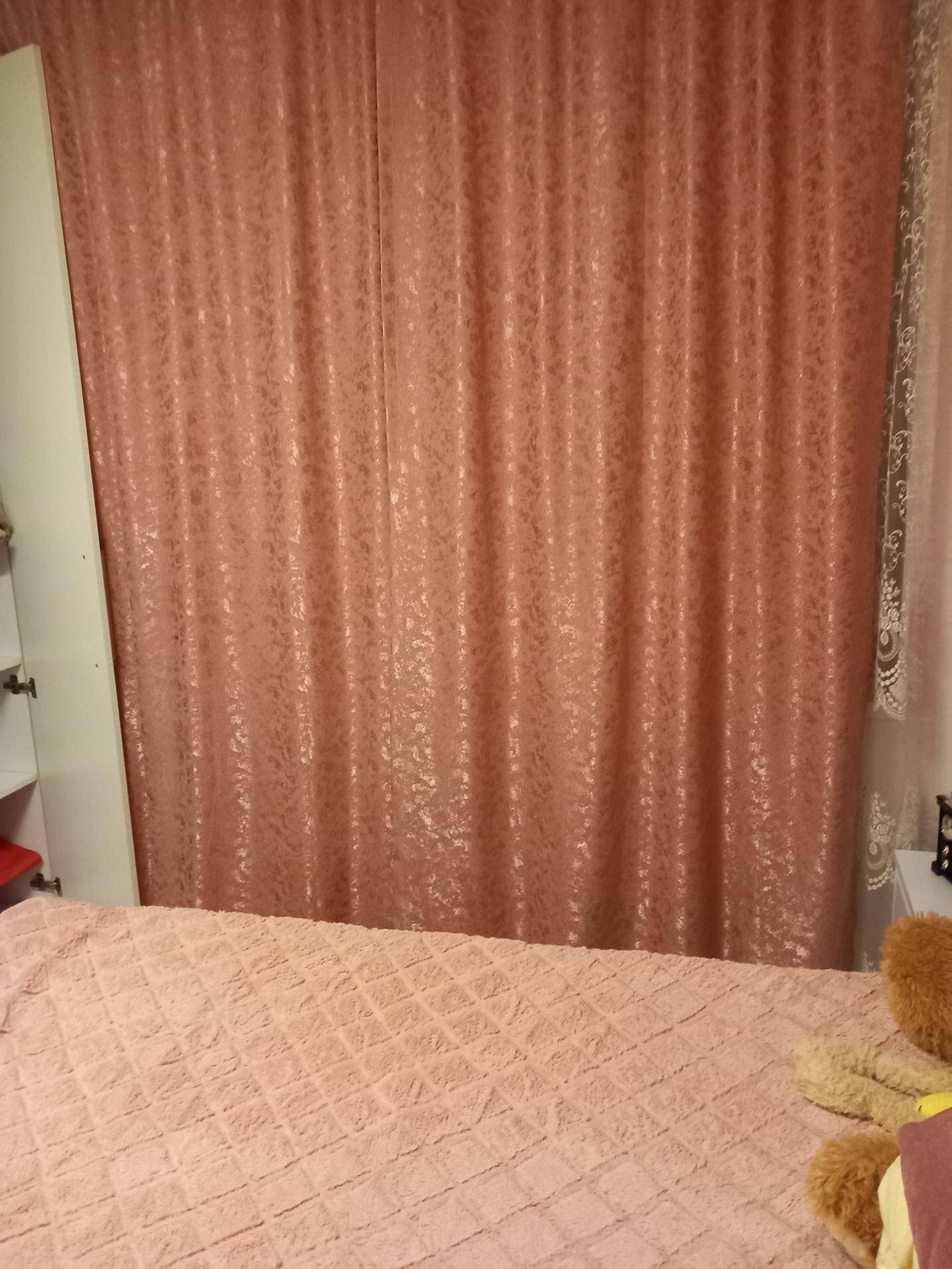 Schlafzimmer mit rosa Vorhängen, die das Fenster bedecken, und einem gemütlichen Bett.