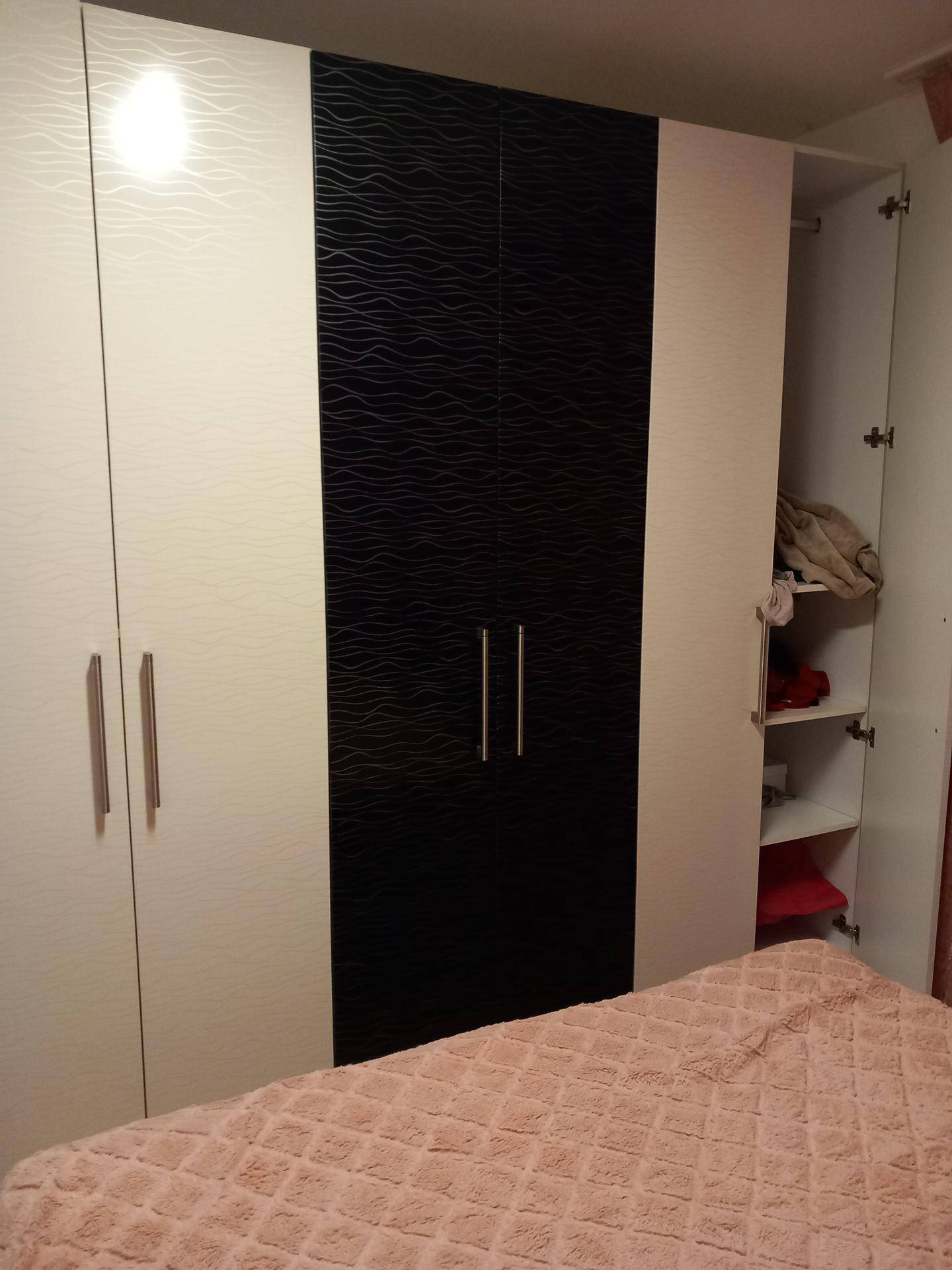 Schlafzimmer mit modernem Kleiderschrank in Weiß und Schwarz neben dem Bett.