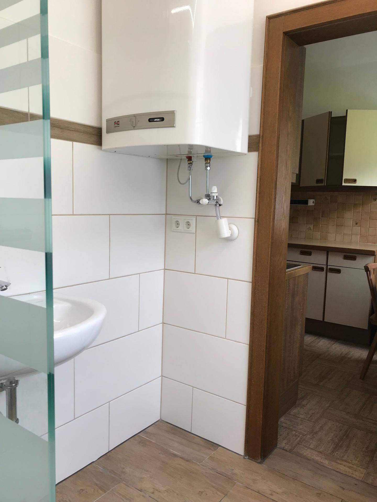 Badezimmer mit Waschbecken, Warmwasserboiler und Zugang zu einer angrenzenden Küche.