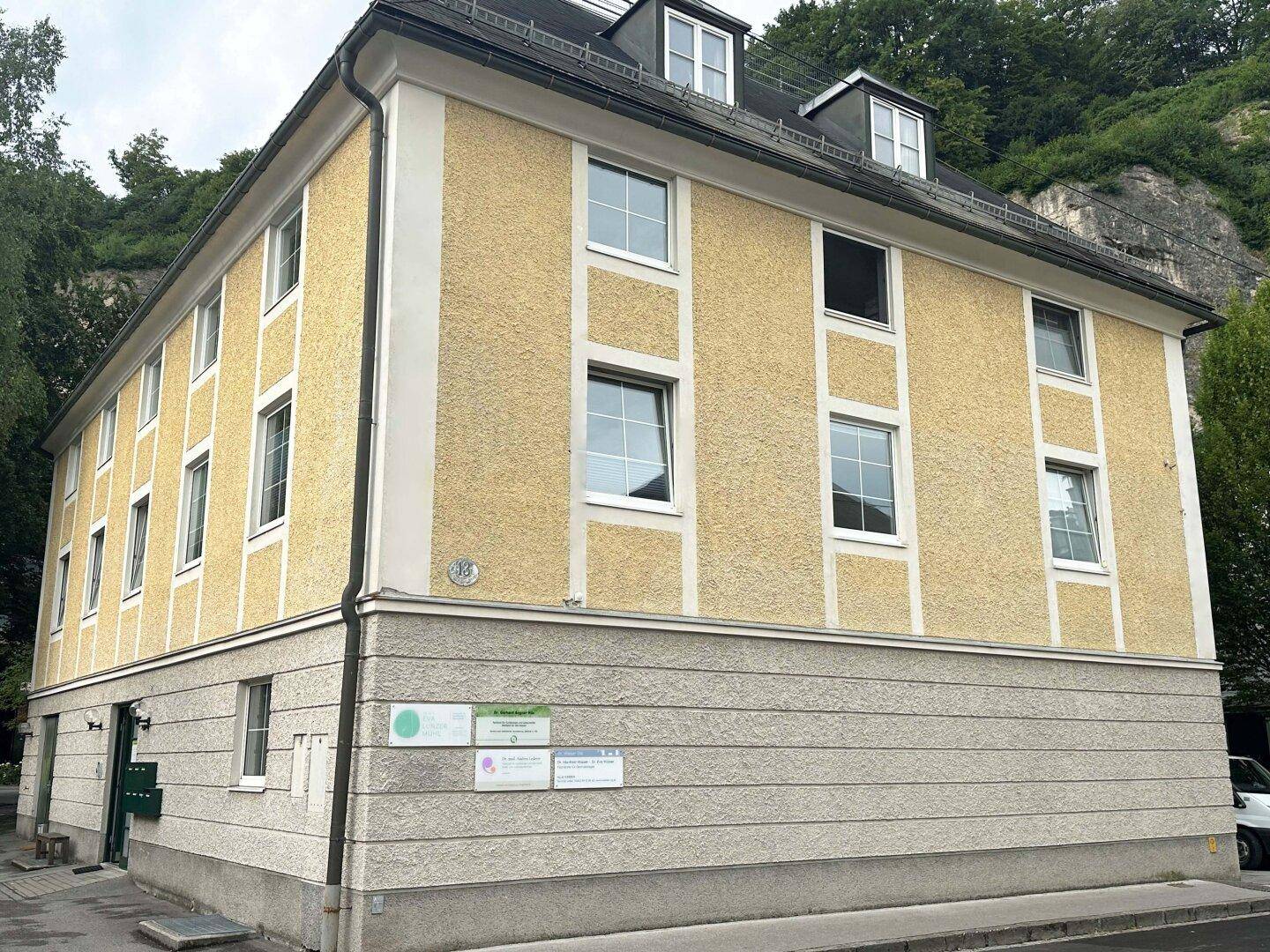 Historisches Gebäude mit gelber Putzfassade und mehreren Fenstern, umgeben von grüner Natur.