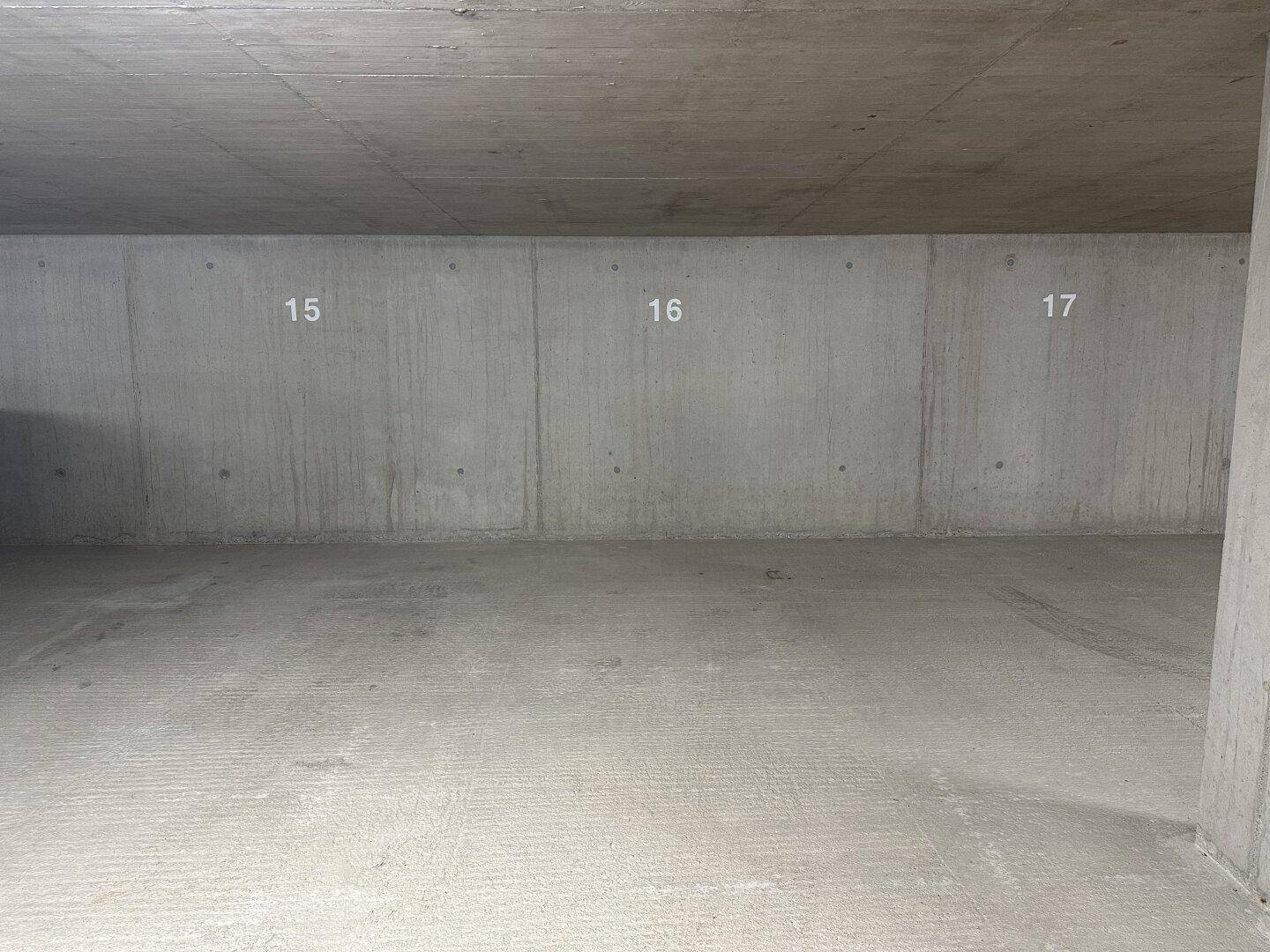 Innenansicht einer Tiefgarage mit Sichtbetonwänden und nummerierten Stellplätzen in sauberem Zustand.