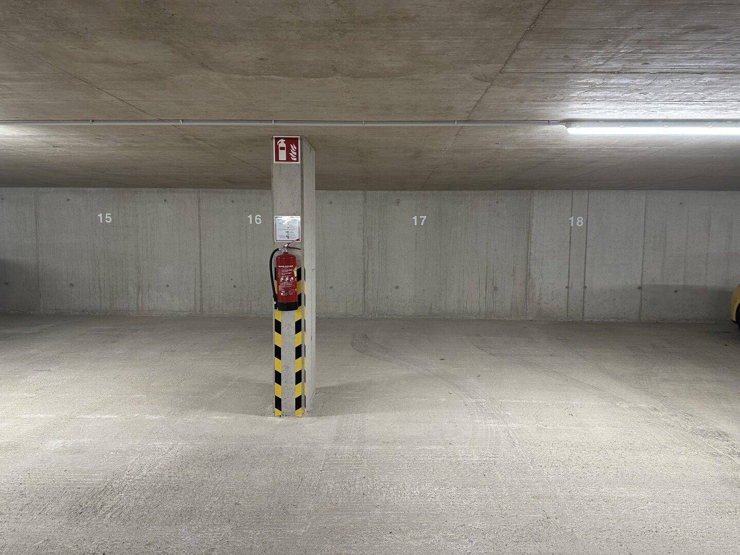 Geräumige Tiefgarage mit Betonpfeiler, Feuerlöscher und klar gekennzeichneten Parkbereichen.