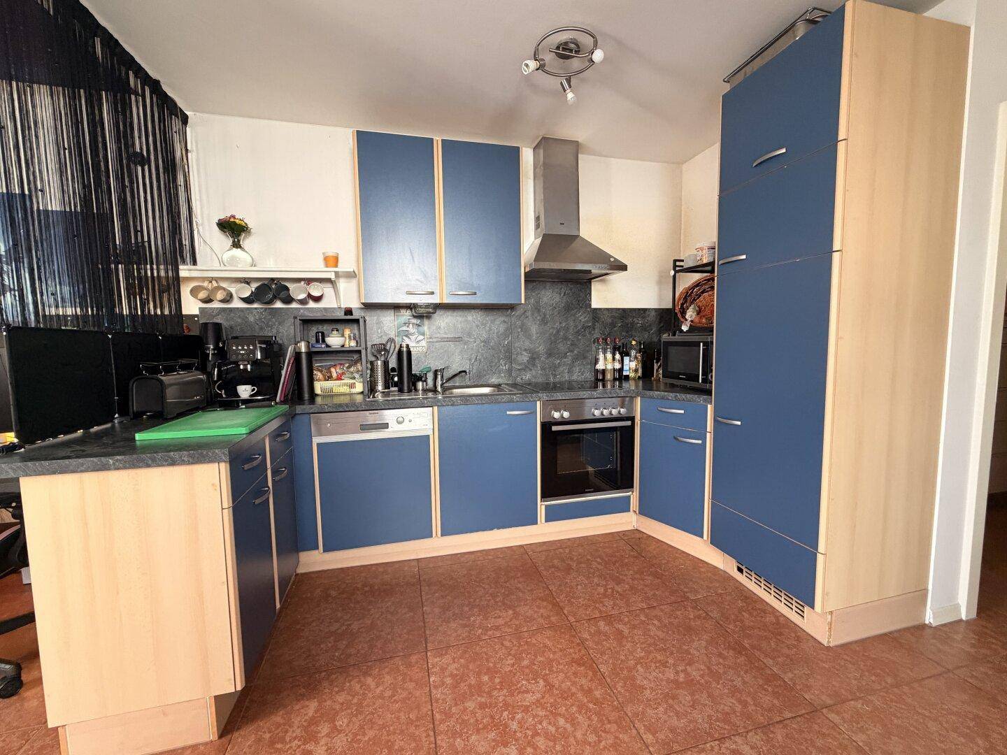 Funktionale Küche mit blauen Schränken, Holzdetails und integrierten Elektrogeräten.