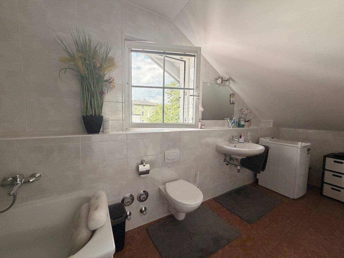 Badezimmer im Dachgeschoss mit Badewanne, WC, Waschbecken und einem Fenster mit Ausblick.