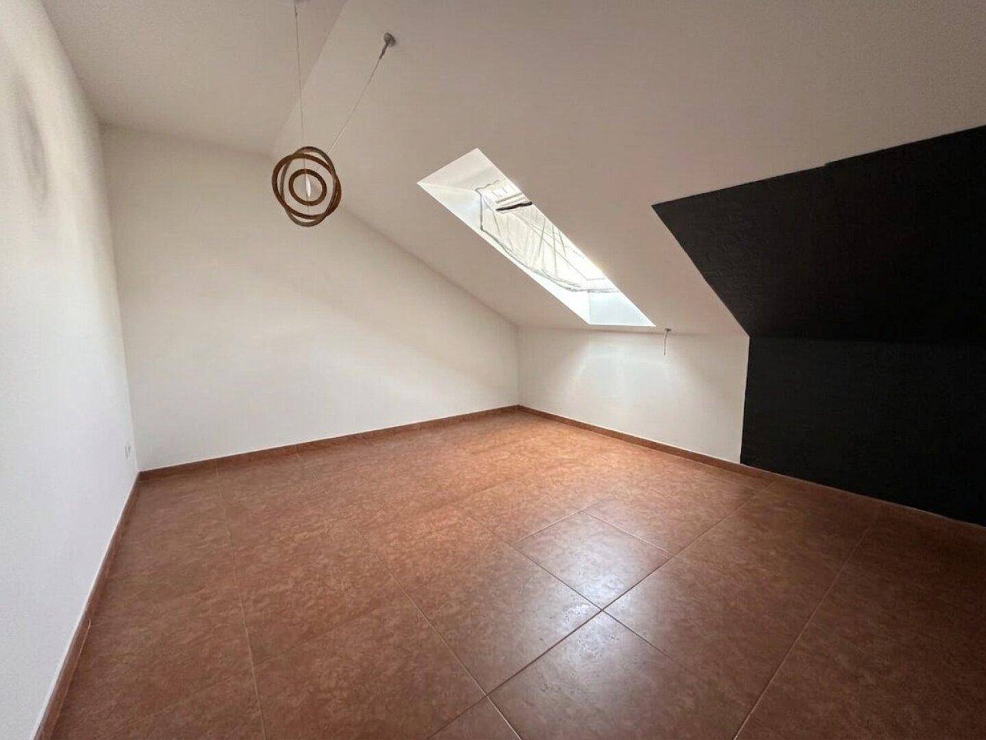 Geräumiges Dachgeschosszimmer mit Dachschräge, Fliesenboden, Oberlicht und dunkler Akzentwand.