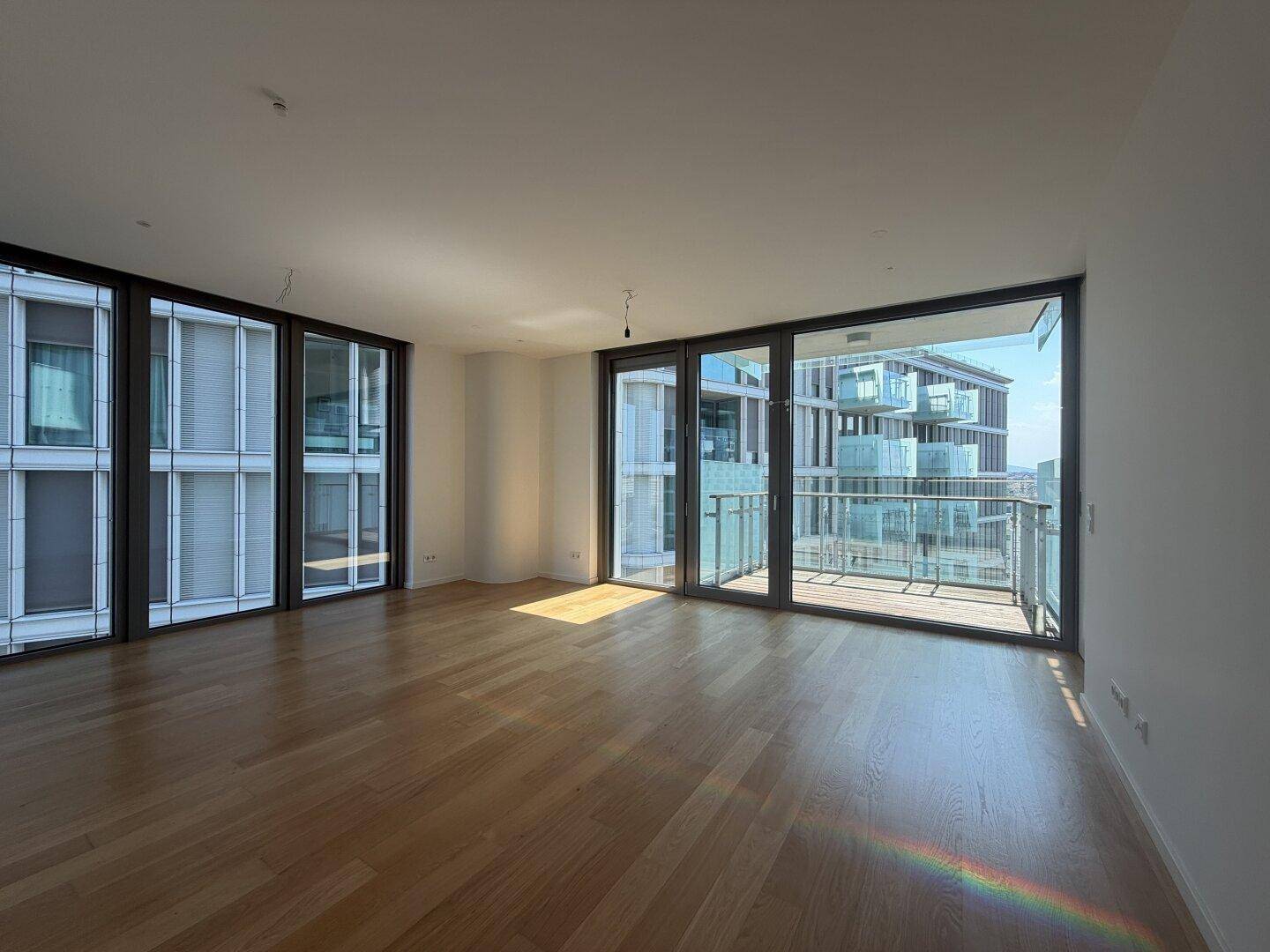 Lichtdurchflutetes Zimmer mit Holzboden und Zugang zu einem Balkon mit urbanem Ausblick.