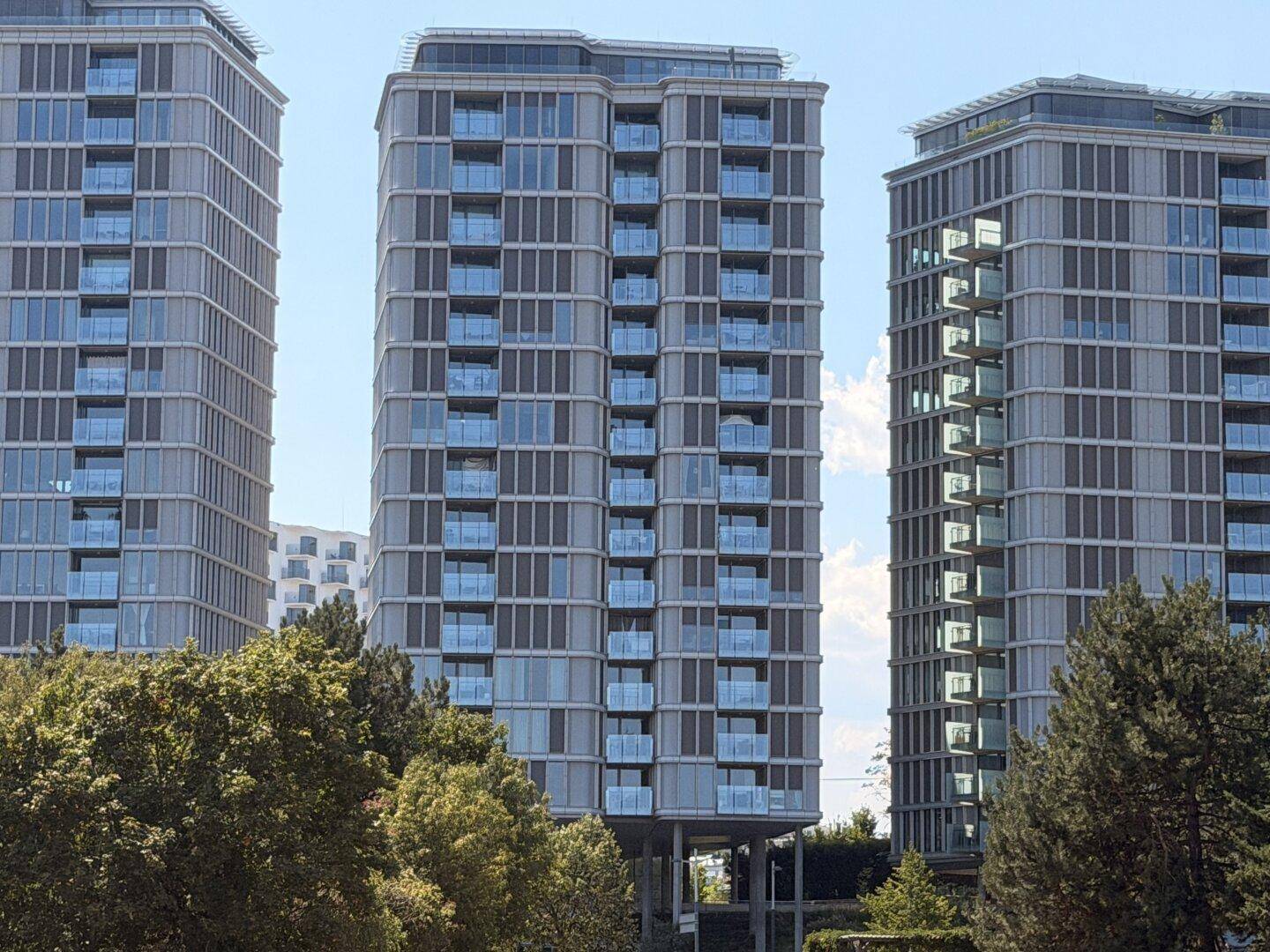 Moderne Hochhäuser mit zahlreichen Balkonen und großen Fensterfronten unter blauem Himmel.