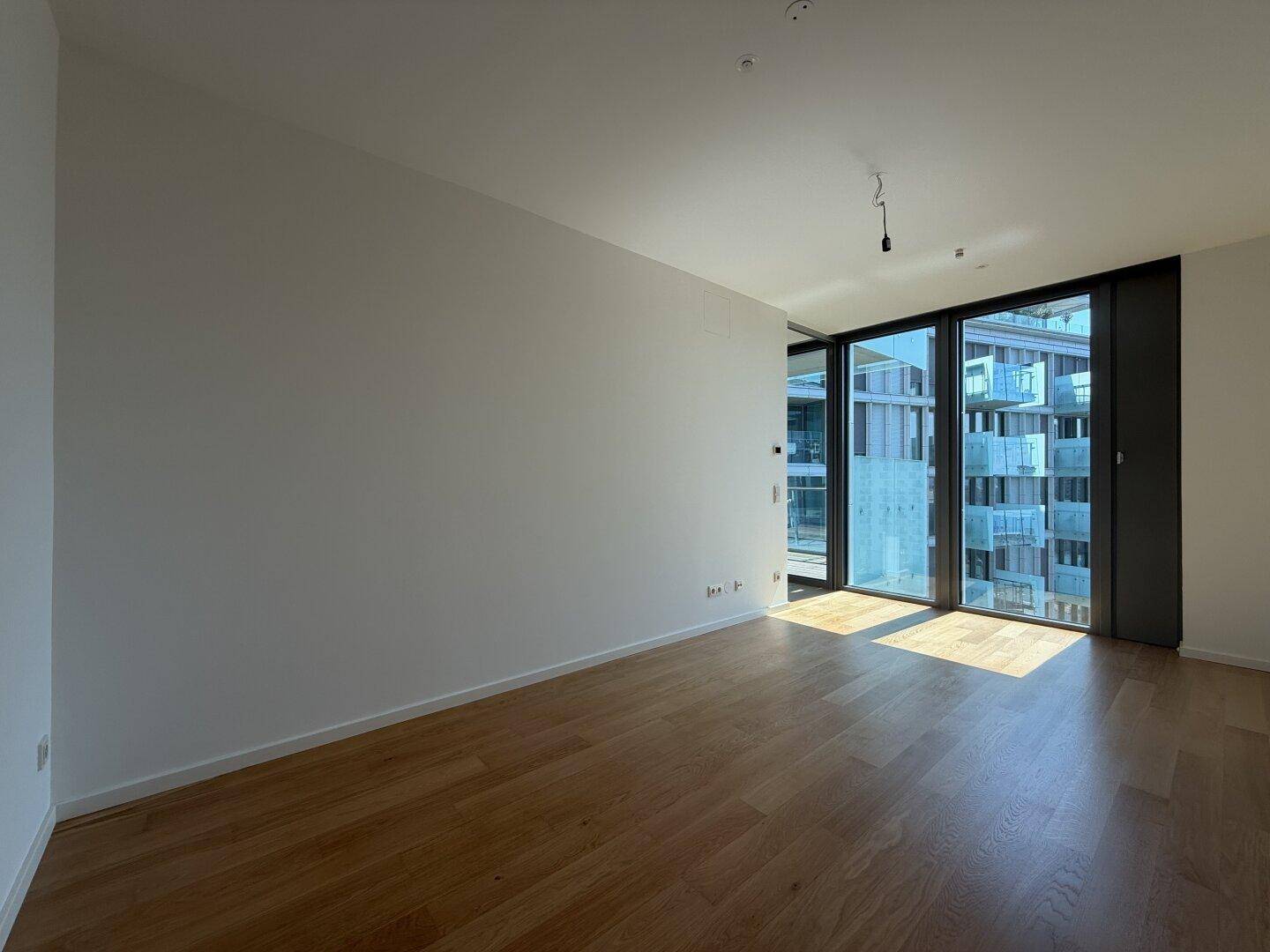 Heller Raum mit Holzboden und großen Fenstern, die viel natürliches Licht hereinlassen.