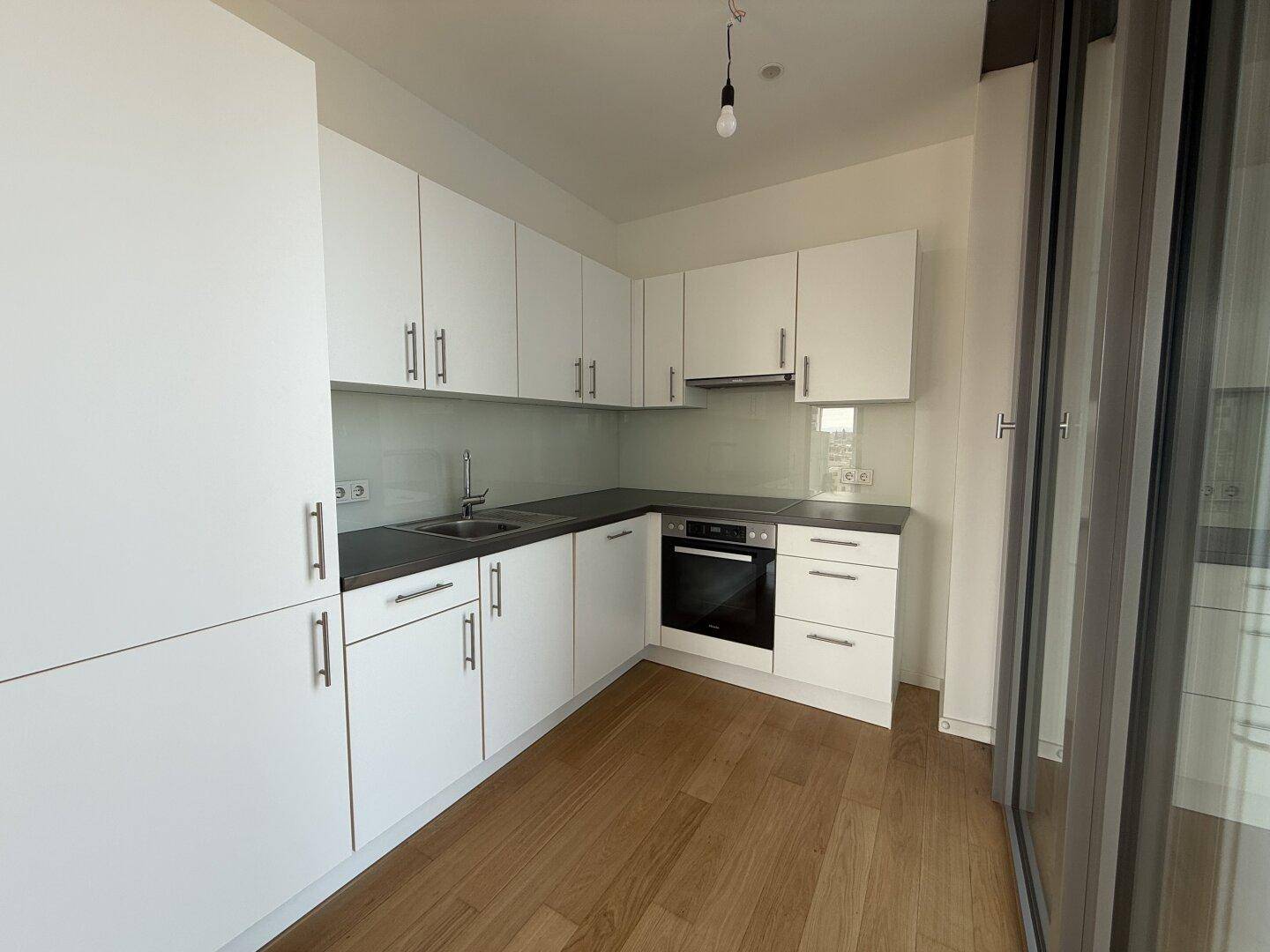 Moderne Einbauküche mit weißen Schränken, dunkler Arbeitsplatte und integrierten Geräten.