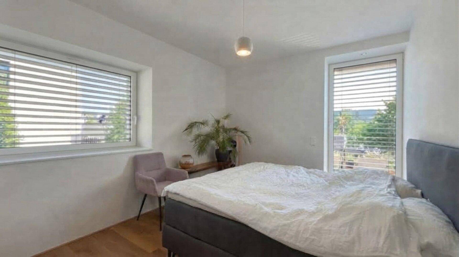 Helles Schlafzimmer mit großen Fenstern, Holzfußboden und Blick ins Grüne, modern eingerichtet.
