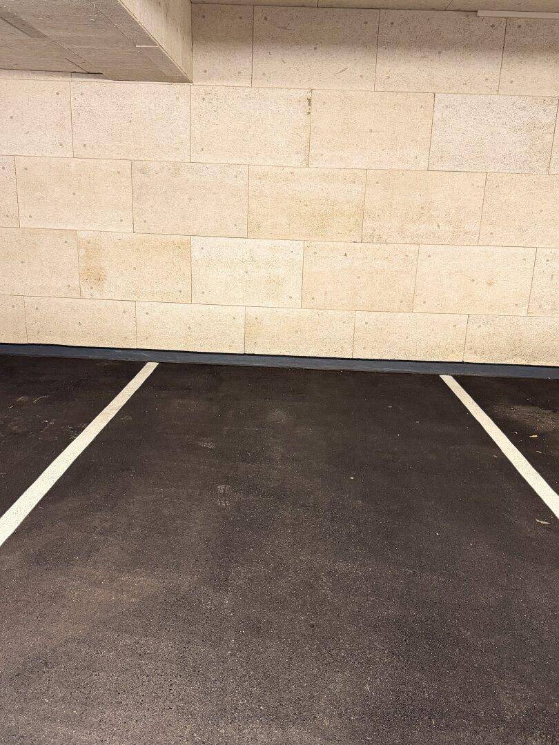 Markierter Parkplatz in einer Tiefgarage mit dunklem Asphaltboden und hellen, strukturierten Steinwänden.
