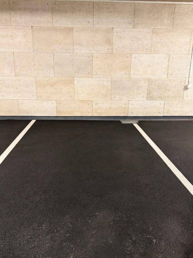 Leerer Parkplatz in einer Tiefgarage mit klaren weißen Markierungen auf dunklem Boden und Steinwand.