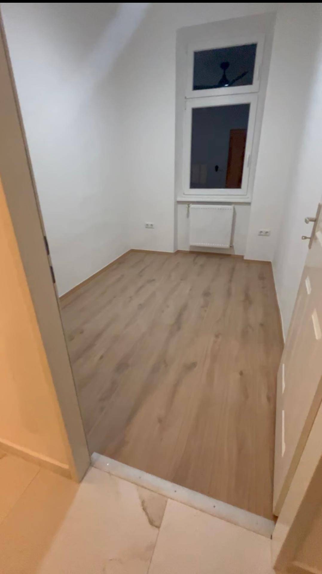 Helles Zimmer mit Laminatboden, weißen Wänden und Fenster, ideal als Schlaf- oder Arbeitszimmer.