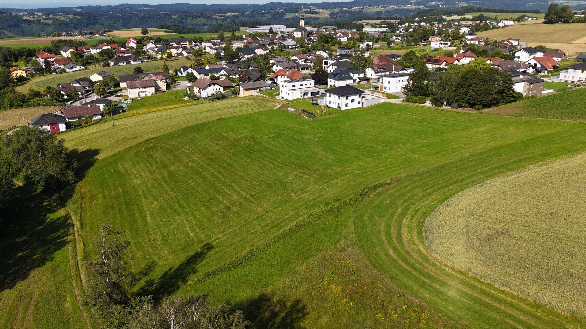 Luftaufnahme einer ländlichen Gegend mit Feldern, Waldstücken und einem Dorf im Hintergrund.
