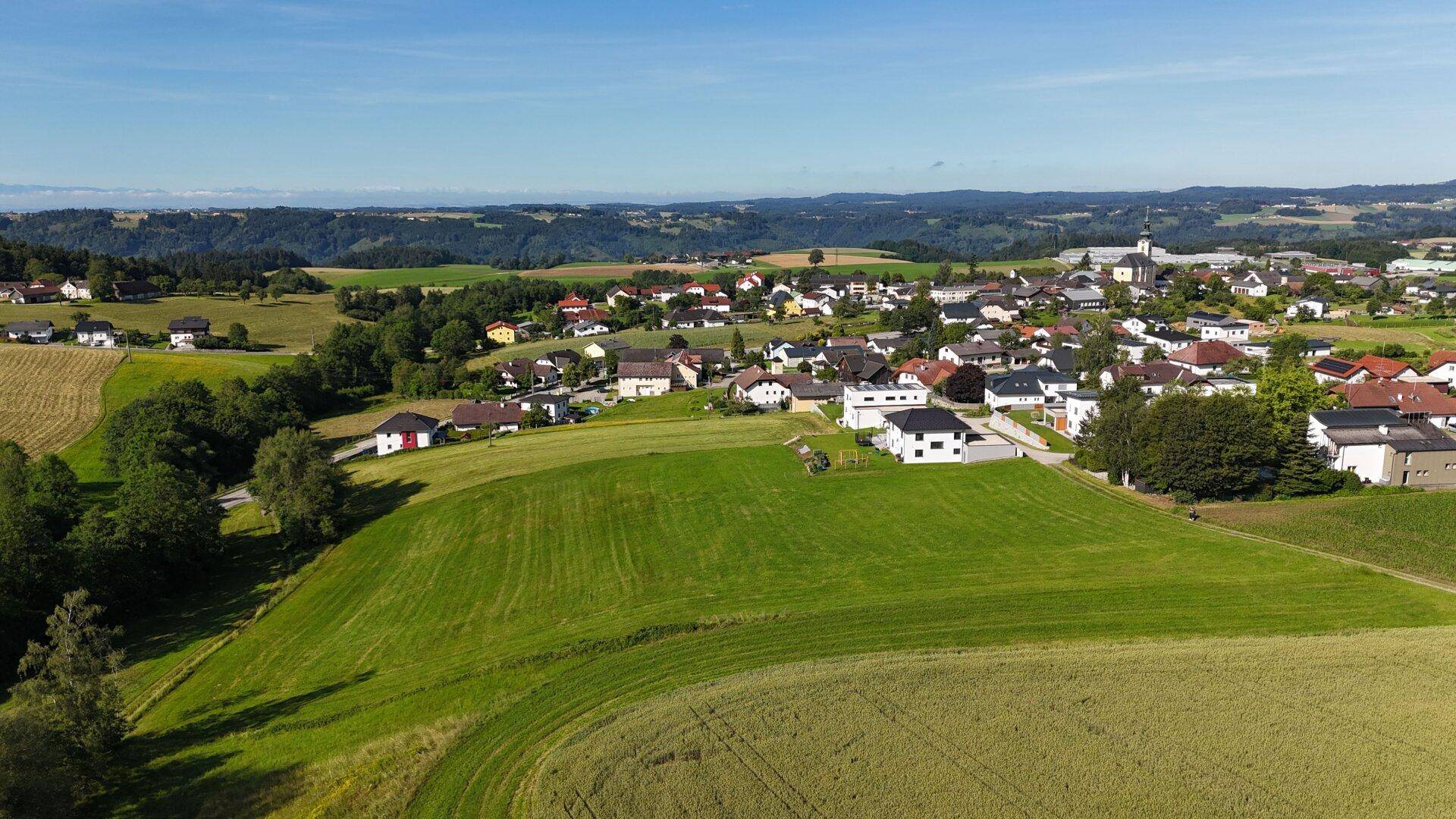 Weitwinkelaufnahme einer idyllischen Landschaft mit Feldern, Häusern und einem Kirchturm in der Ferne.