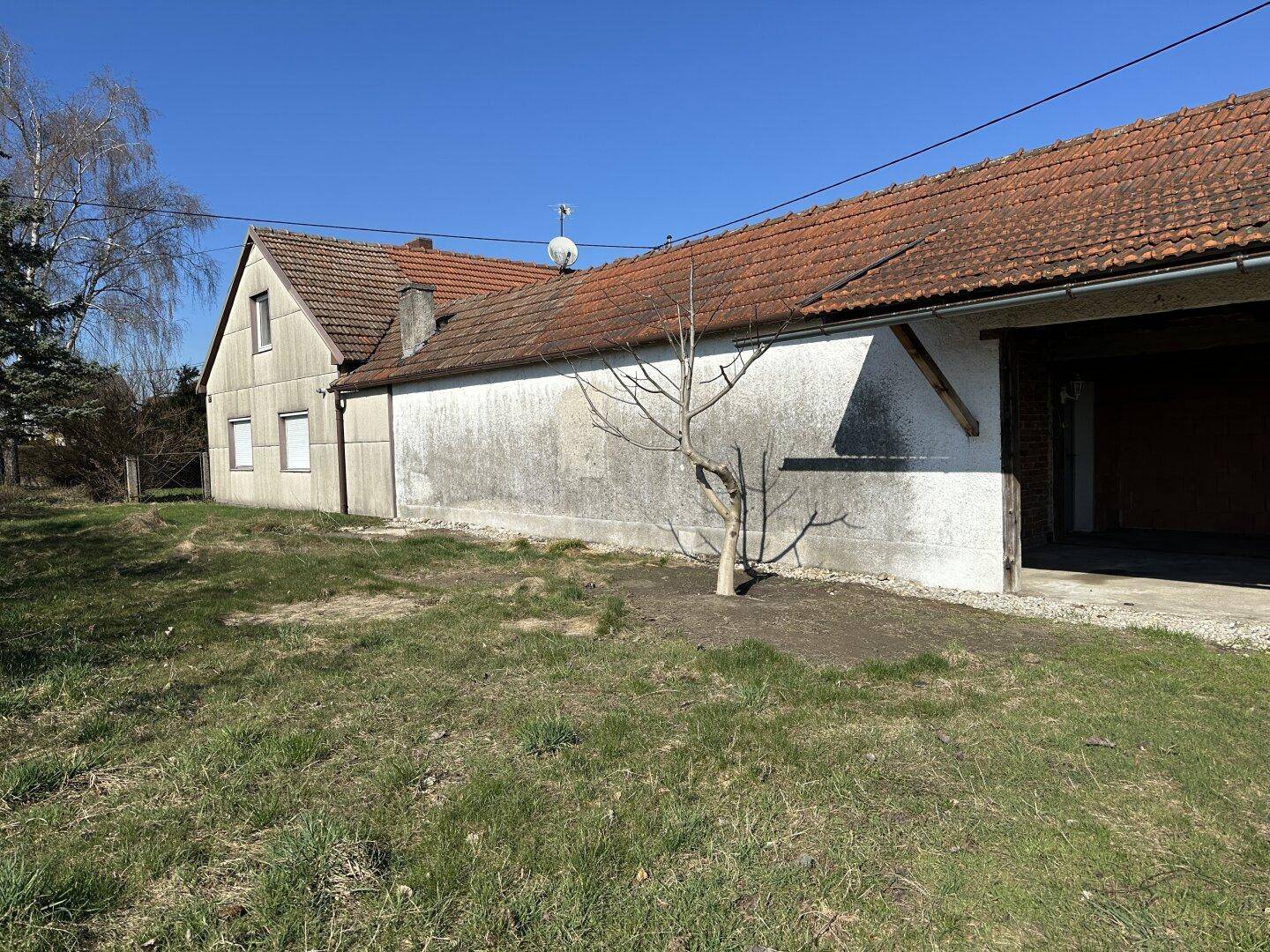 Seitenansicht des Hauses mit angrenzendem Scheunenbereich und großem, ungenutztem Garten.