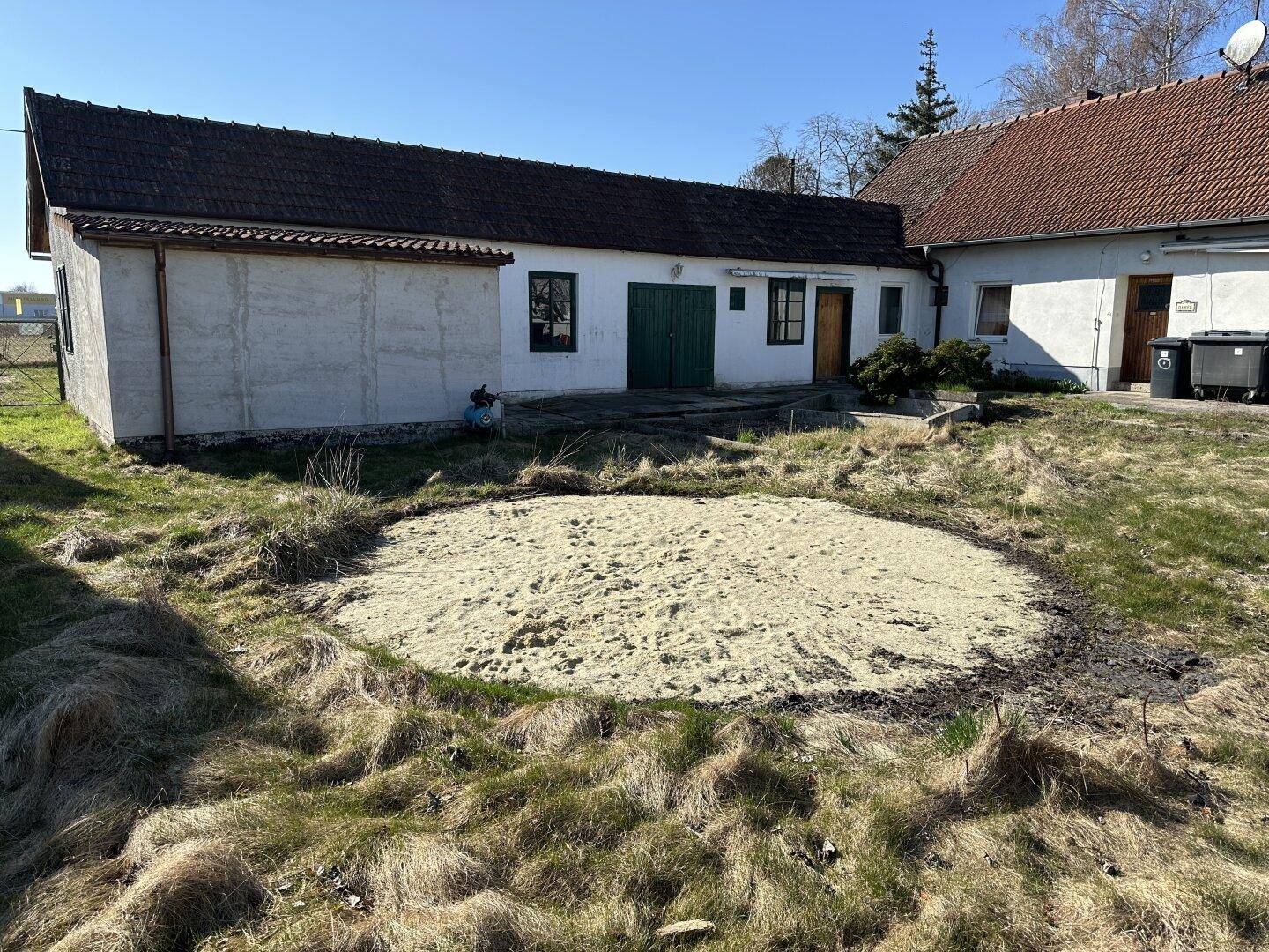 Gartenansicht des Anwesens mit dem Hauptgebäude und einer runden, sandigen Fläche im Rasen.