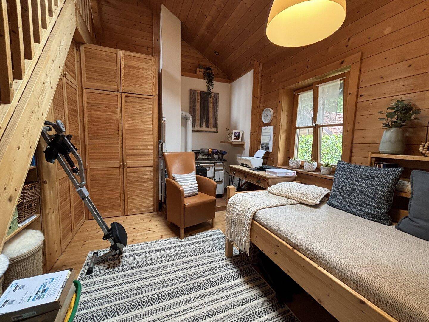 Vielseitiger Raum mit Holzwänden, Schreibtisch, Schlafsofa und Fitnessgerät.