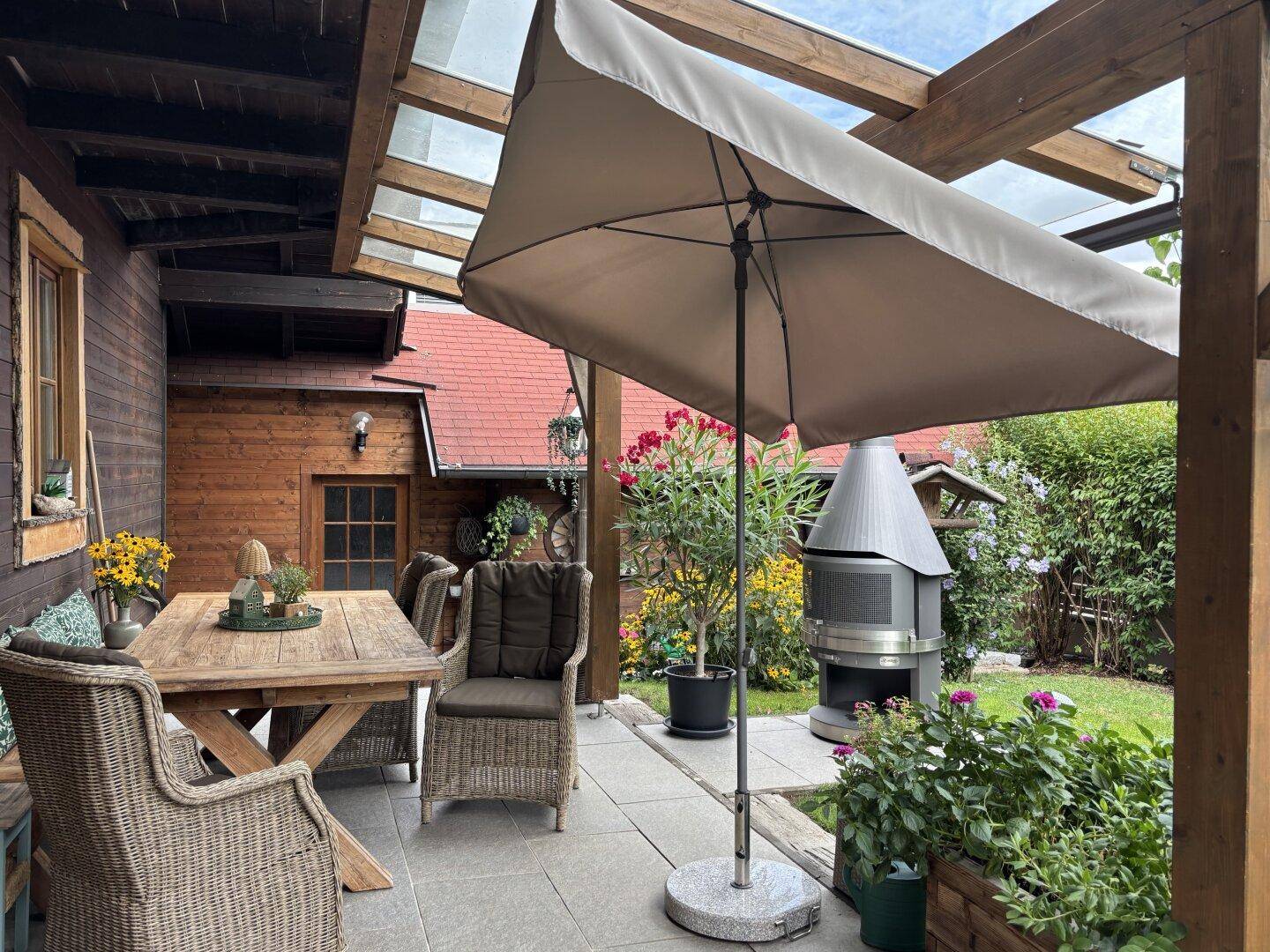 Überdachte Terrasse mit Gartenmöbeln, Grillplatz und Blick ins Grüne.