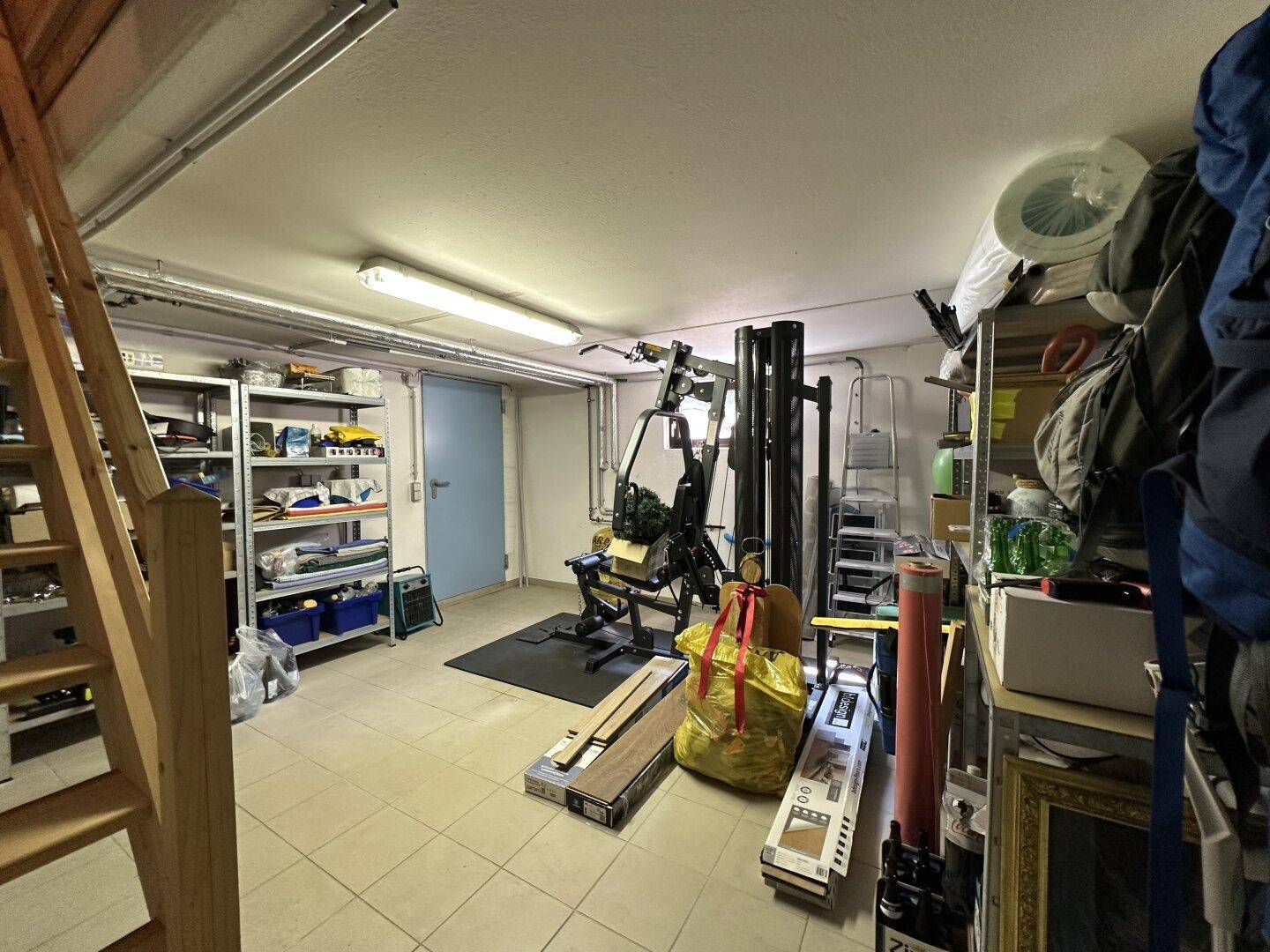 Geräumiger Kellerraum mit Lagerregalen, Fitnessgeräten und Holztreppe.