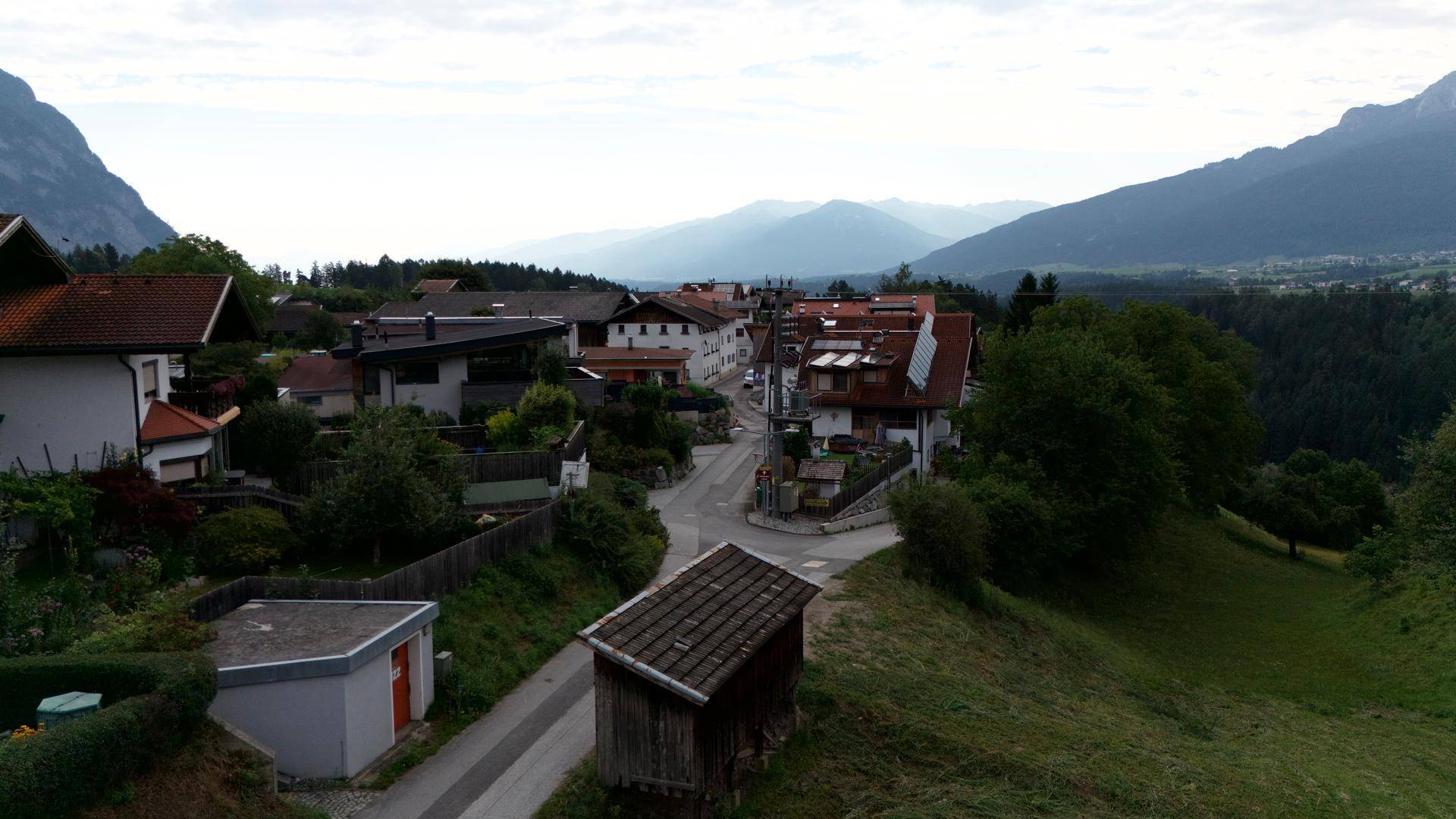 Blick auf eine ruhige Dorfstraße mit traditionellen Häusern und einer malerischen Bergkulisse.