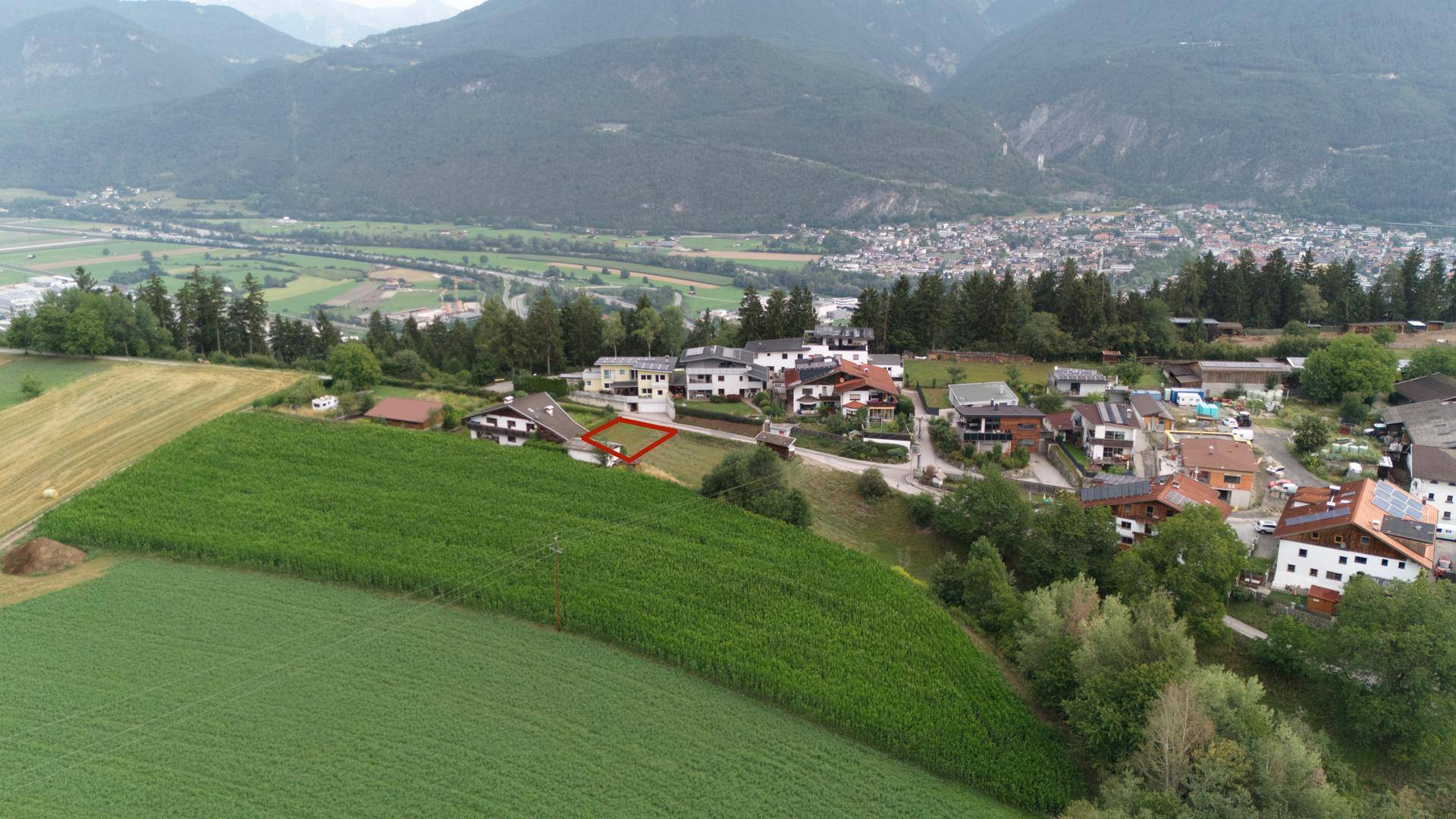 Panoramablick auf ein Dorf am Hang mit weiten Feldern und einer Bergkulisse im Hintergrund.
