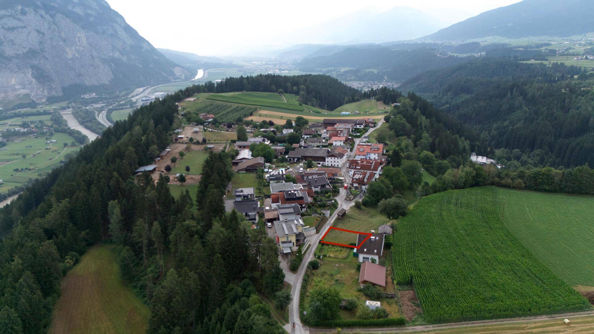 Weitläufige Luftaufnahme eines Dorfes in einem Tal, umgeben von Bergen und Feldern.
