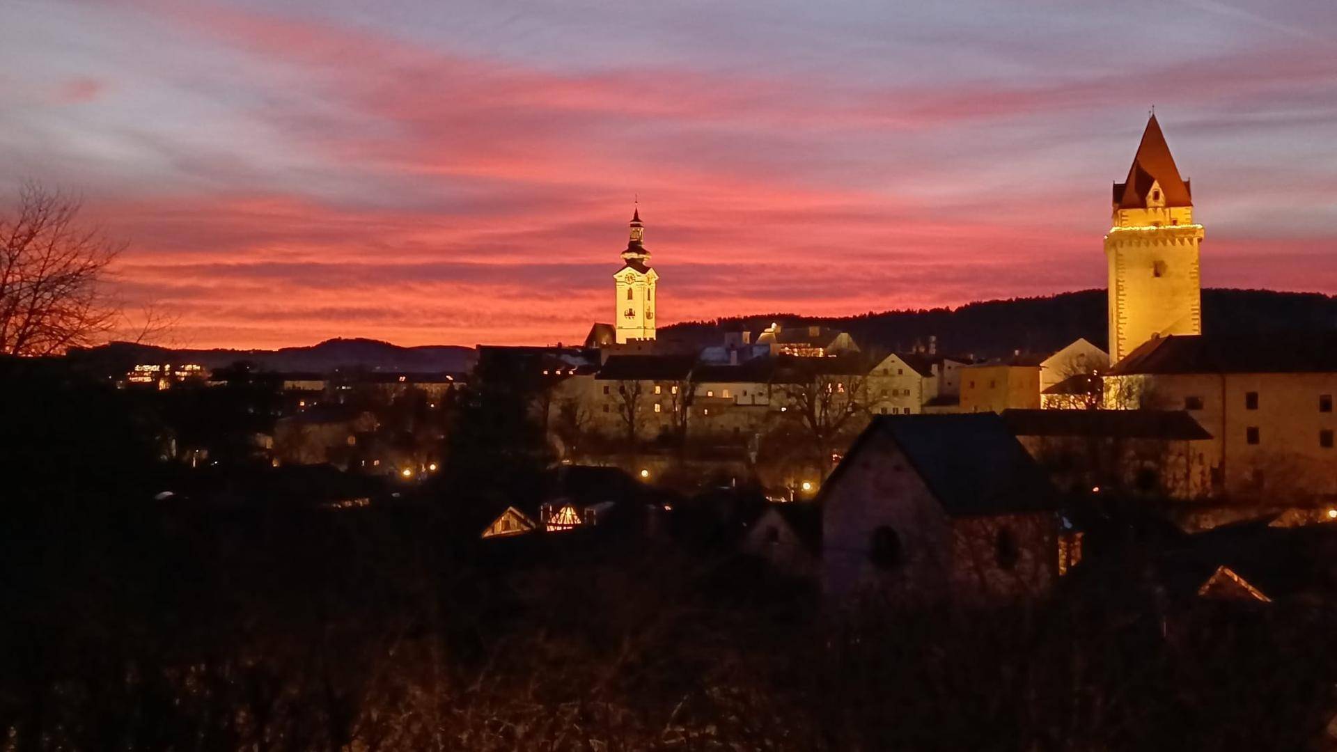 Spektakulärer Sonnenuntergang über der beleuchteten Stadt mit ihren historischen Türmen.