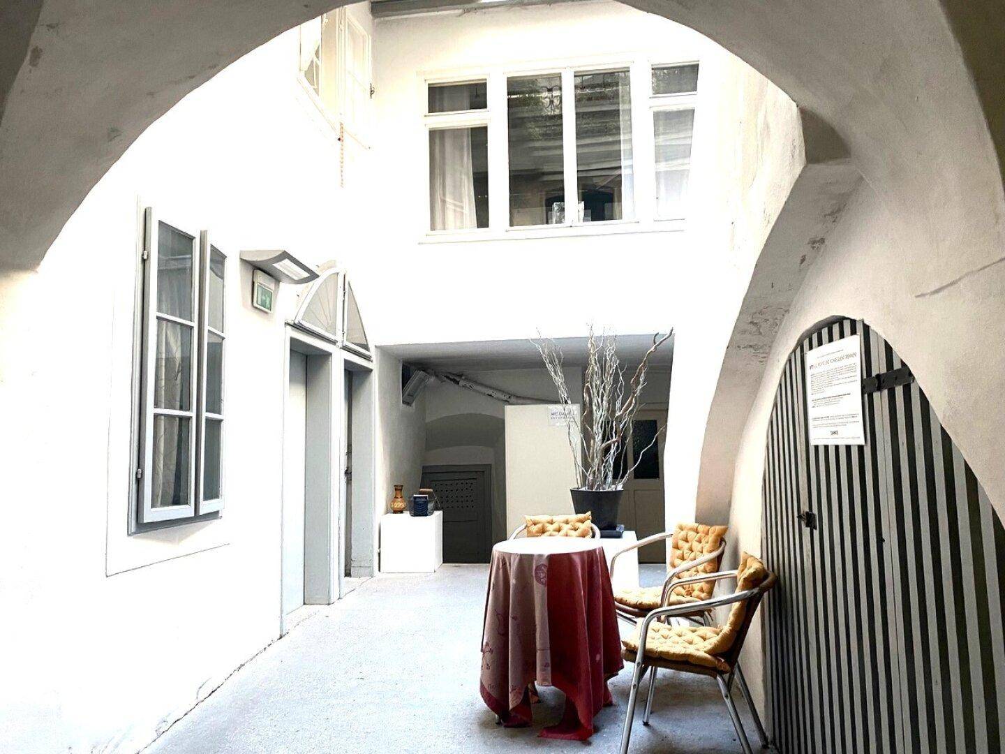 Heller Innenhof mit Arkaden, Fenstern und einem kleinen Tisch mit Stühlen.