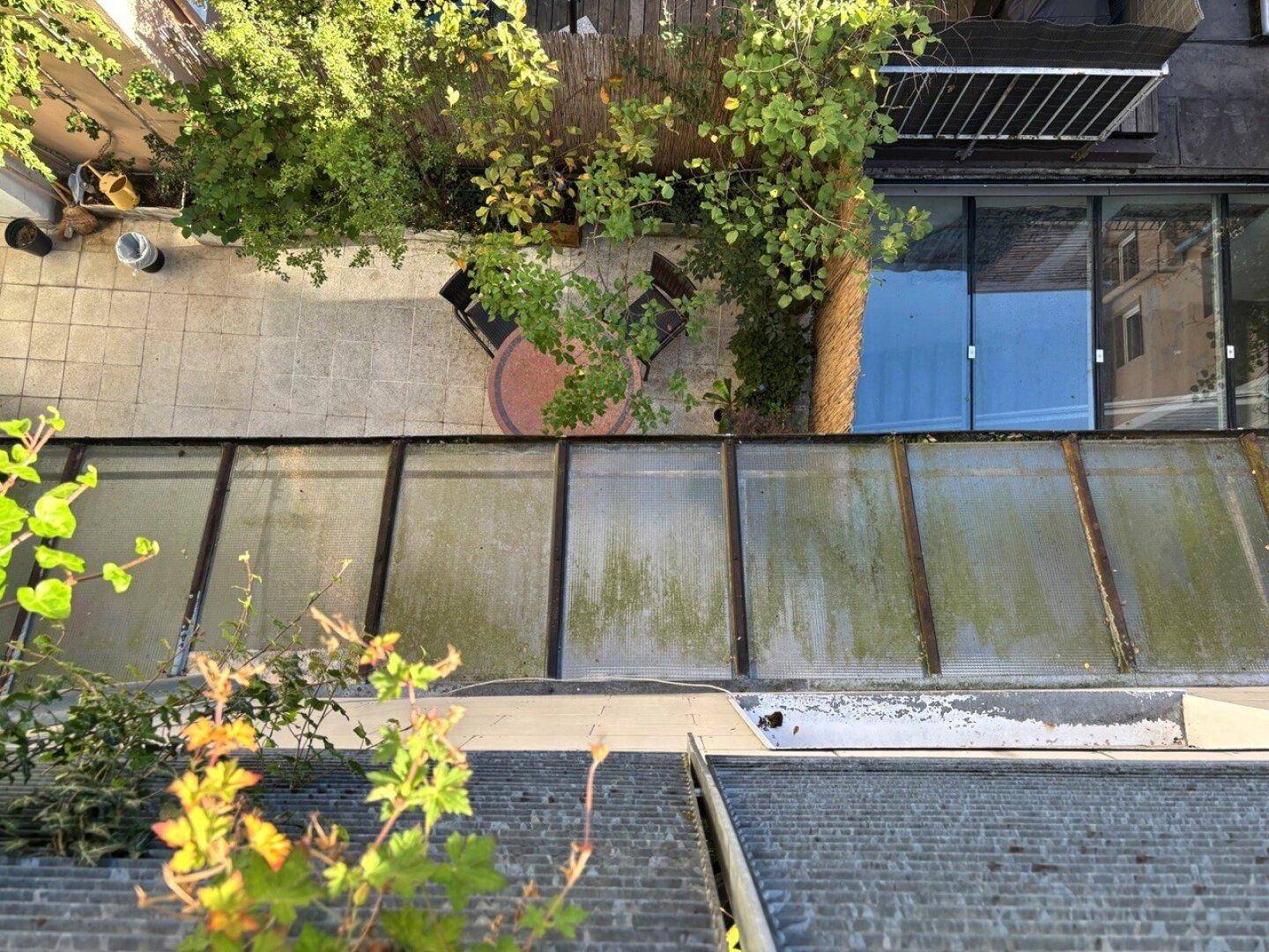 Blick von oben auf eine gepflasterte Terrasse mit einem kleinen Tisch und Stühlen im Freien.
