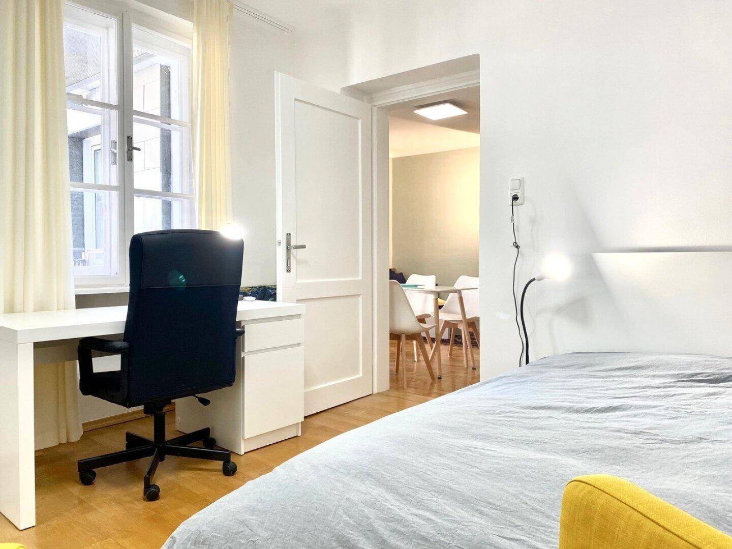 Helles Schlafzimmer mit Holzboden, einem Schreibtisch und einem großen Fenster.