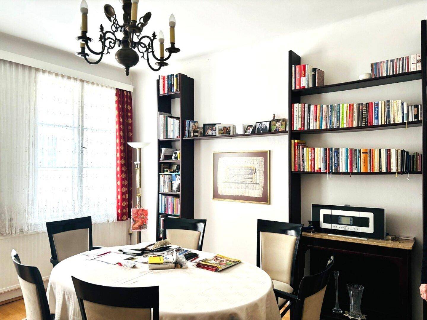 Esszimmer mit rundem Tisch, Bücherregalen und einem klassischen Kronleuchter.