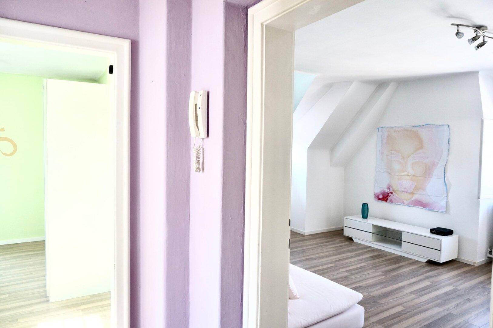 Flur mit gestreifter Wand und Blick in einen Raum mit Dachschräge.